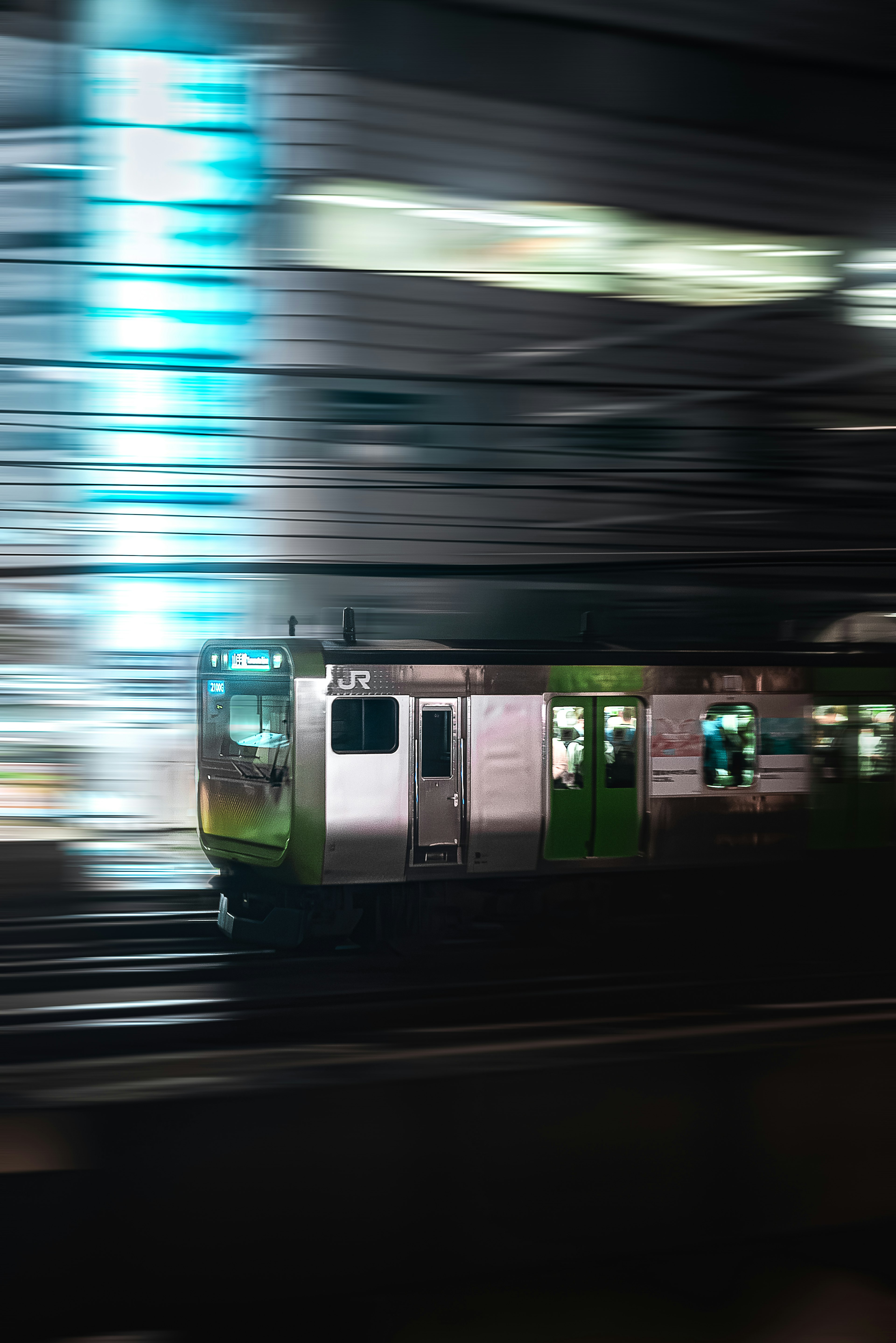 A green train in motion against a blurred city background at night