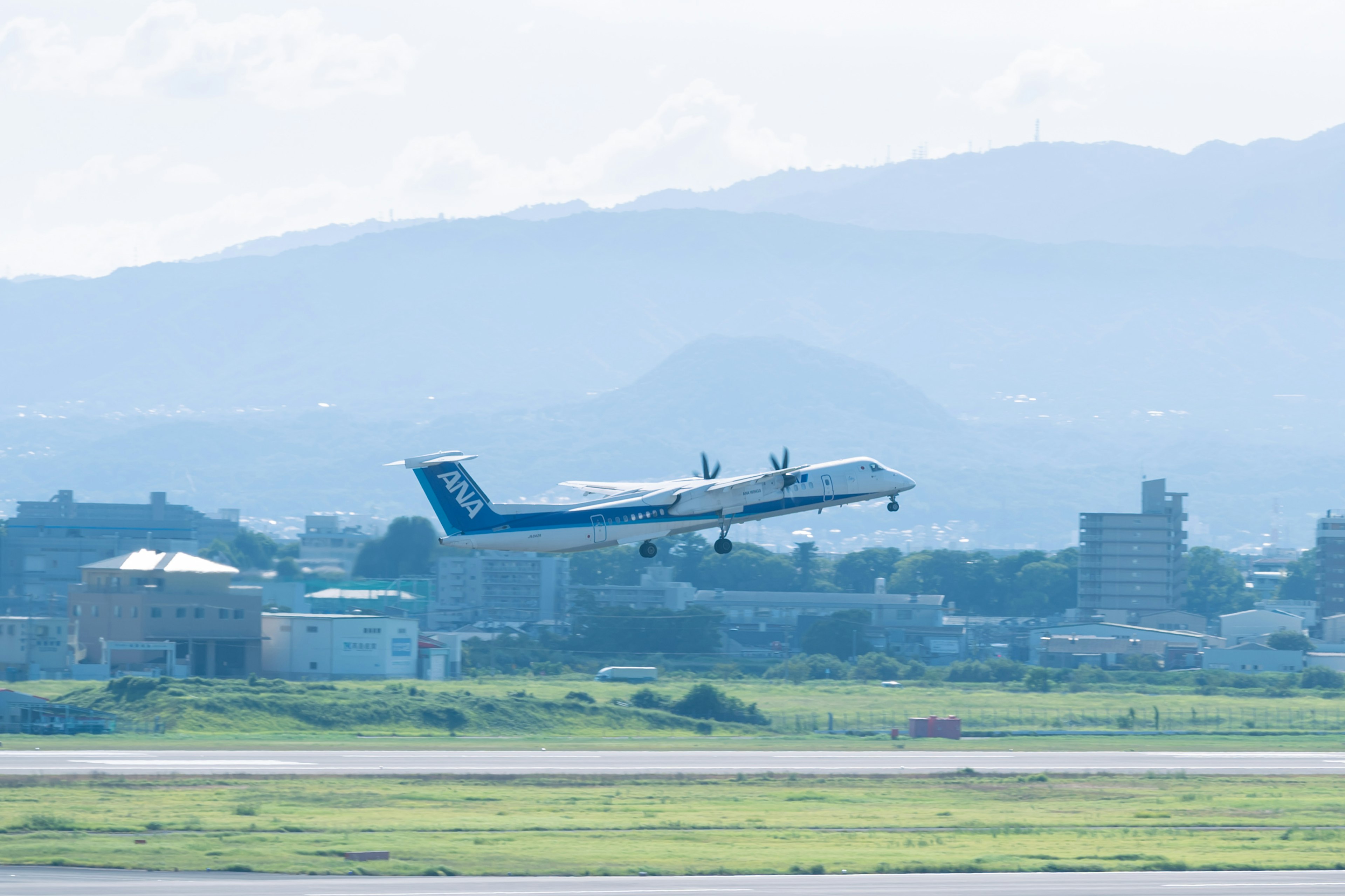 空港で離陸する航空機の写真 青い尾翼と緑の草地が特徴