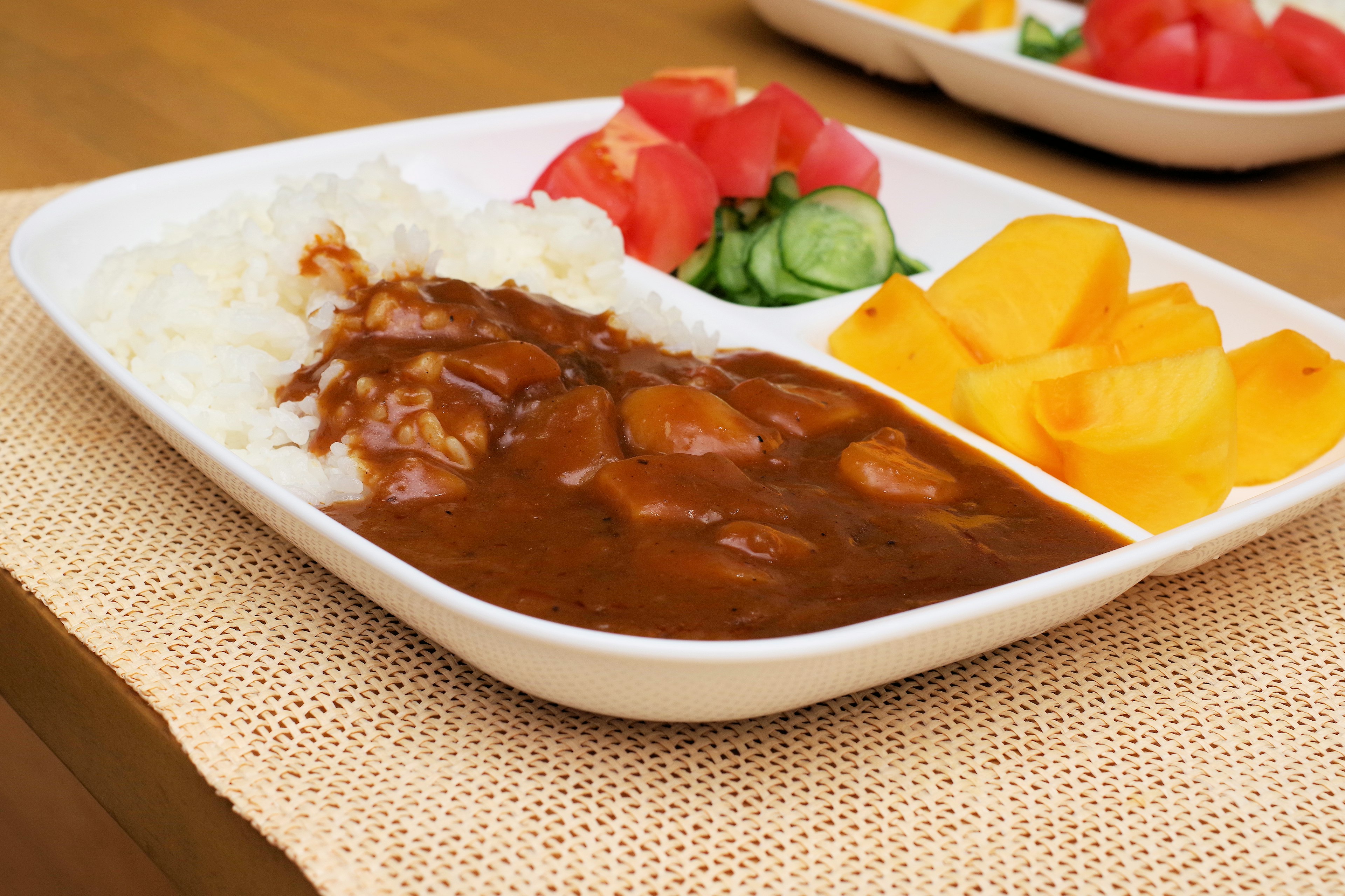 Curry rice served on a white plate with side fruits and vegetables