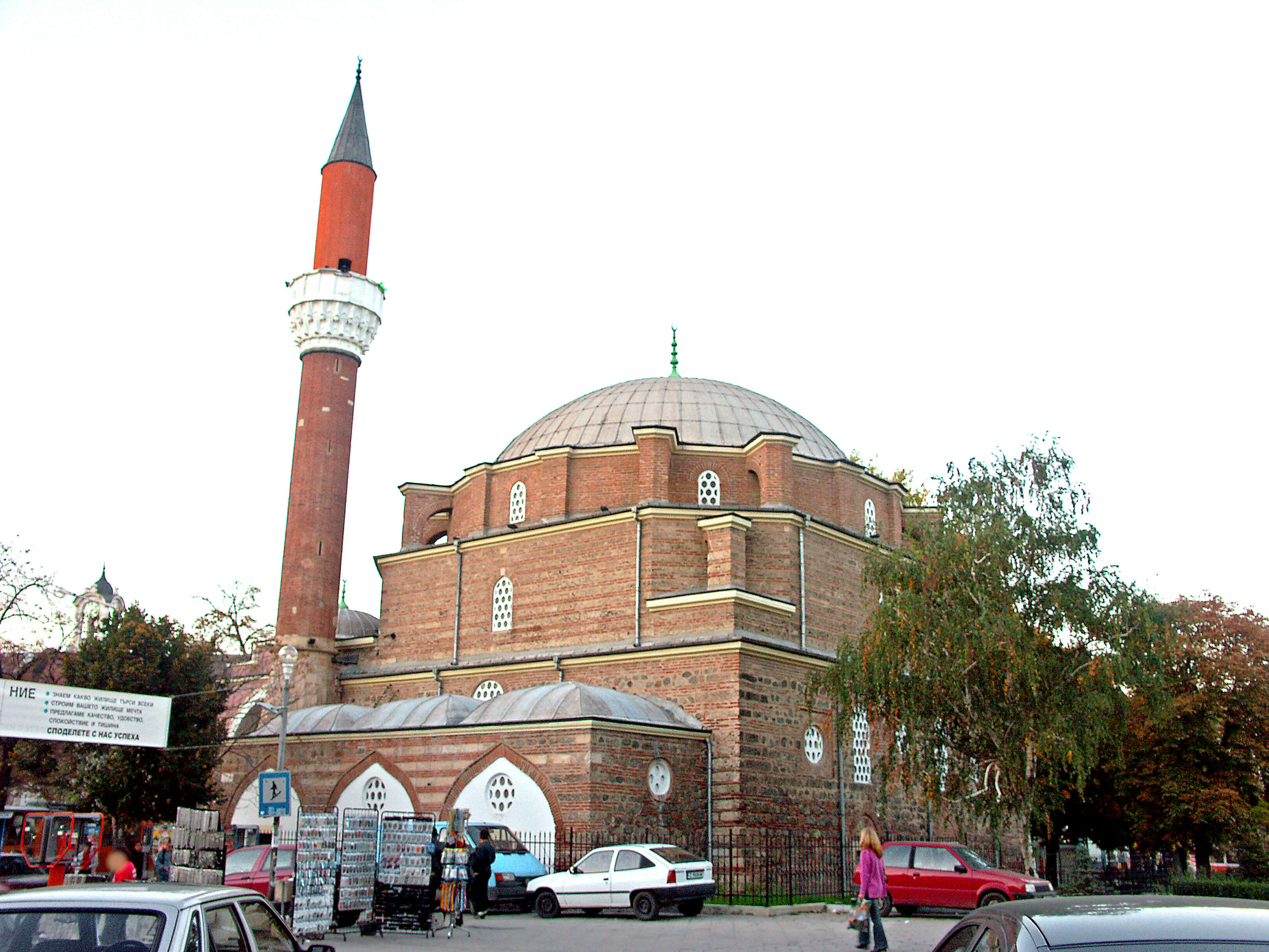 Historische Moschee mit rotem Minarett umgeben von Autos und Bäumen