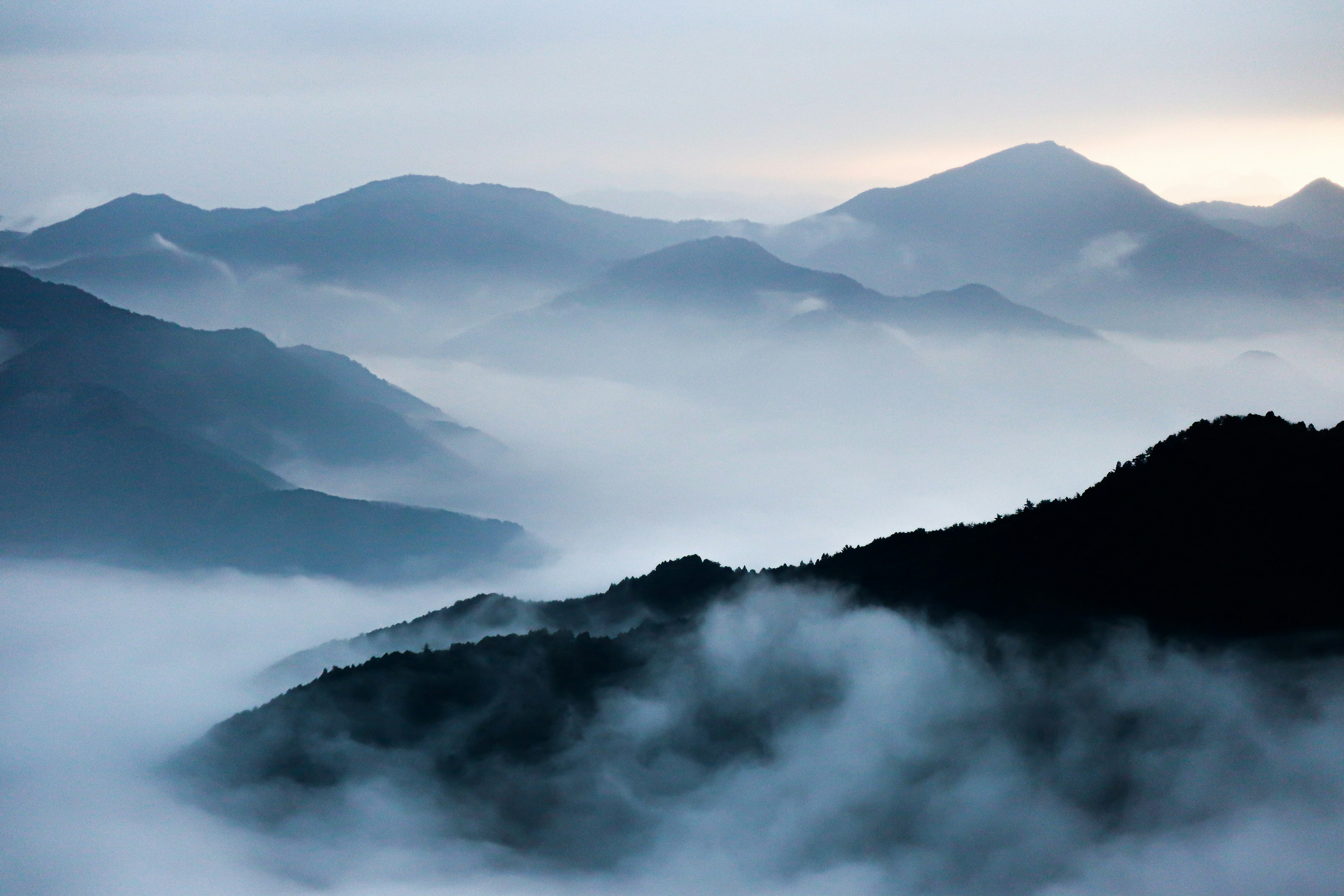 Paesaggio montano avvolto nella nebbia con vette sovrapposte sotto un cielo tenue