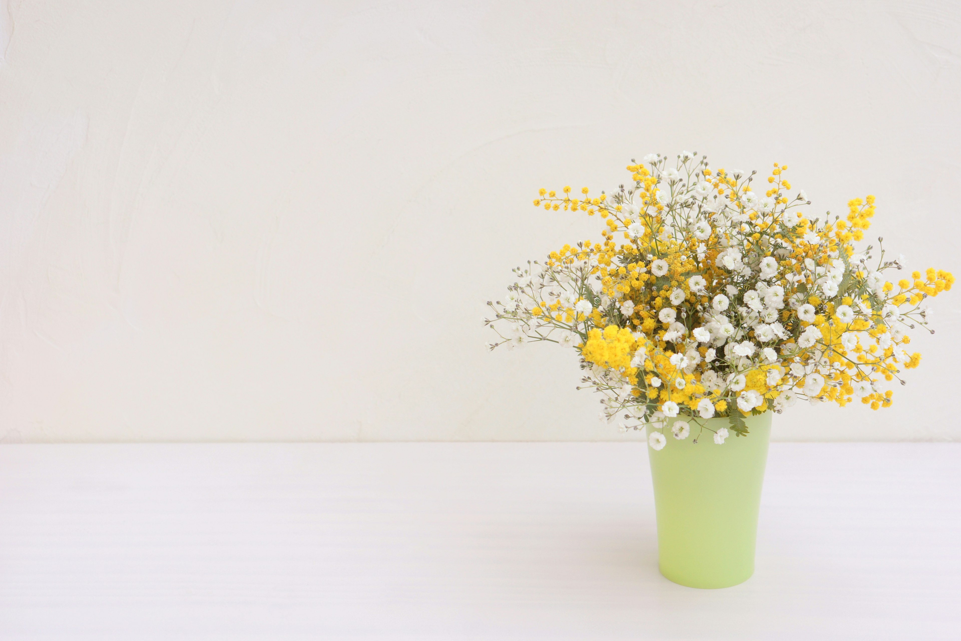 Une image simple d'un vase vert rempli de fleurs jaunes sur un fond clair