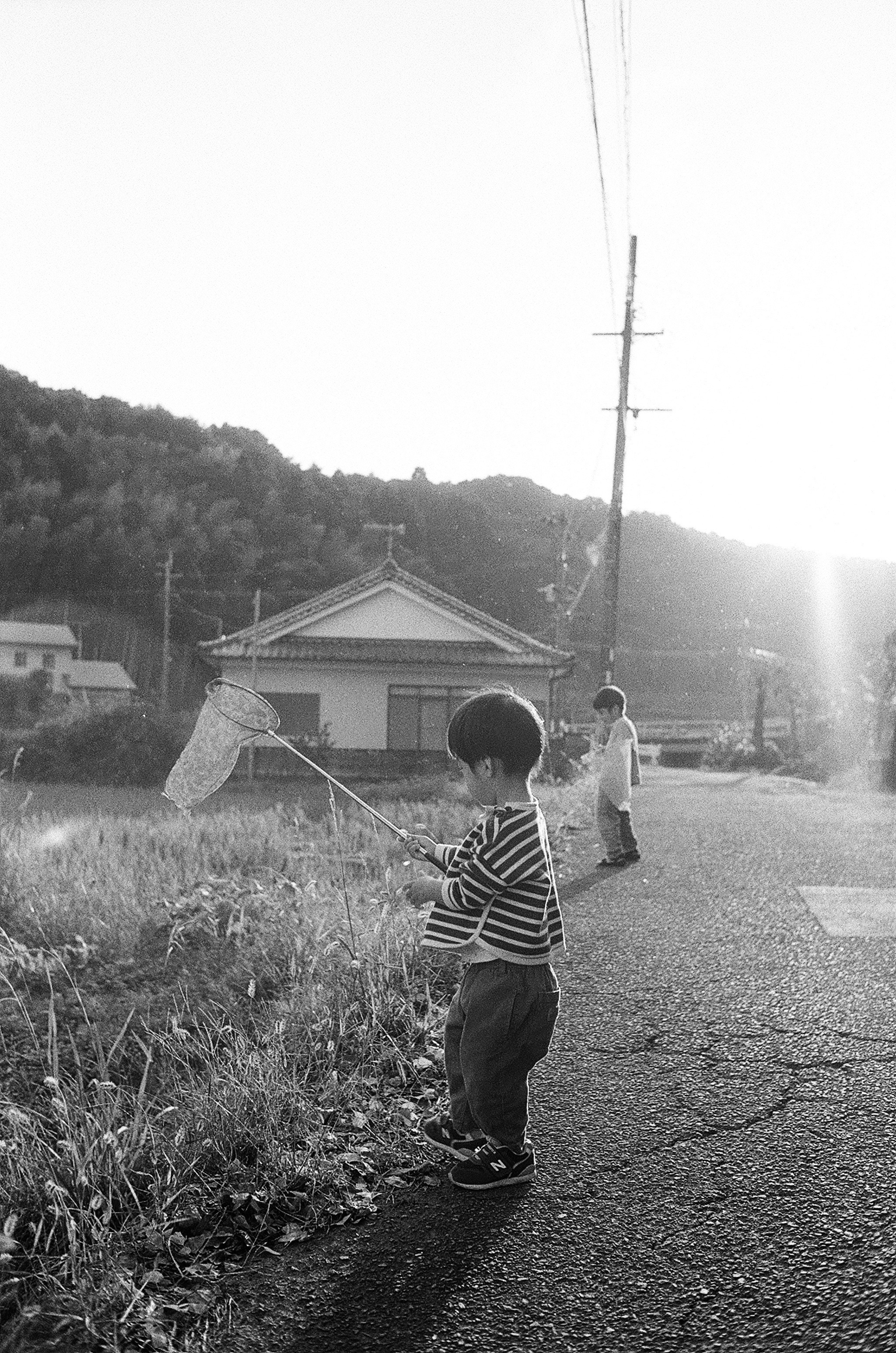 Escena en blanco y negro de un niño con ropa a rayas sosteniendo una red para mariposas