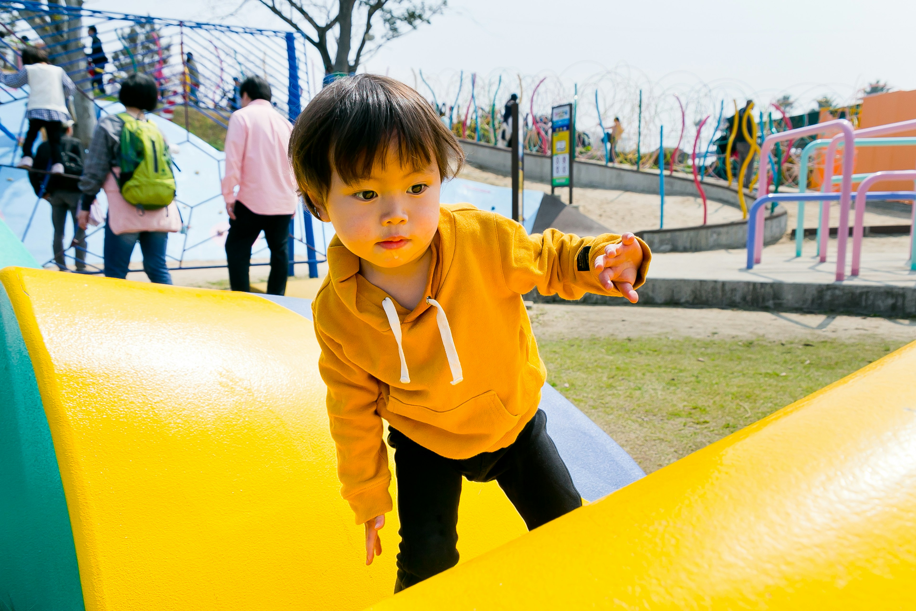 Child playing in a park wearing an orange hoodie climbing on a colorful slide