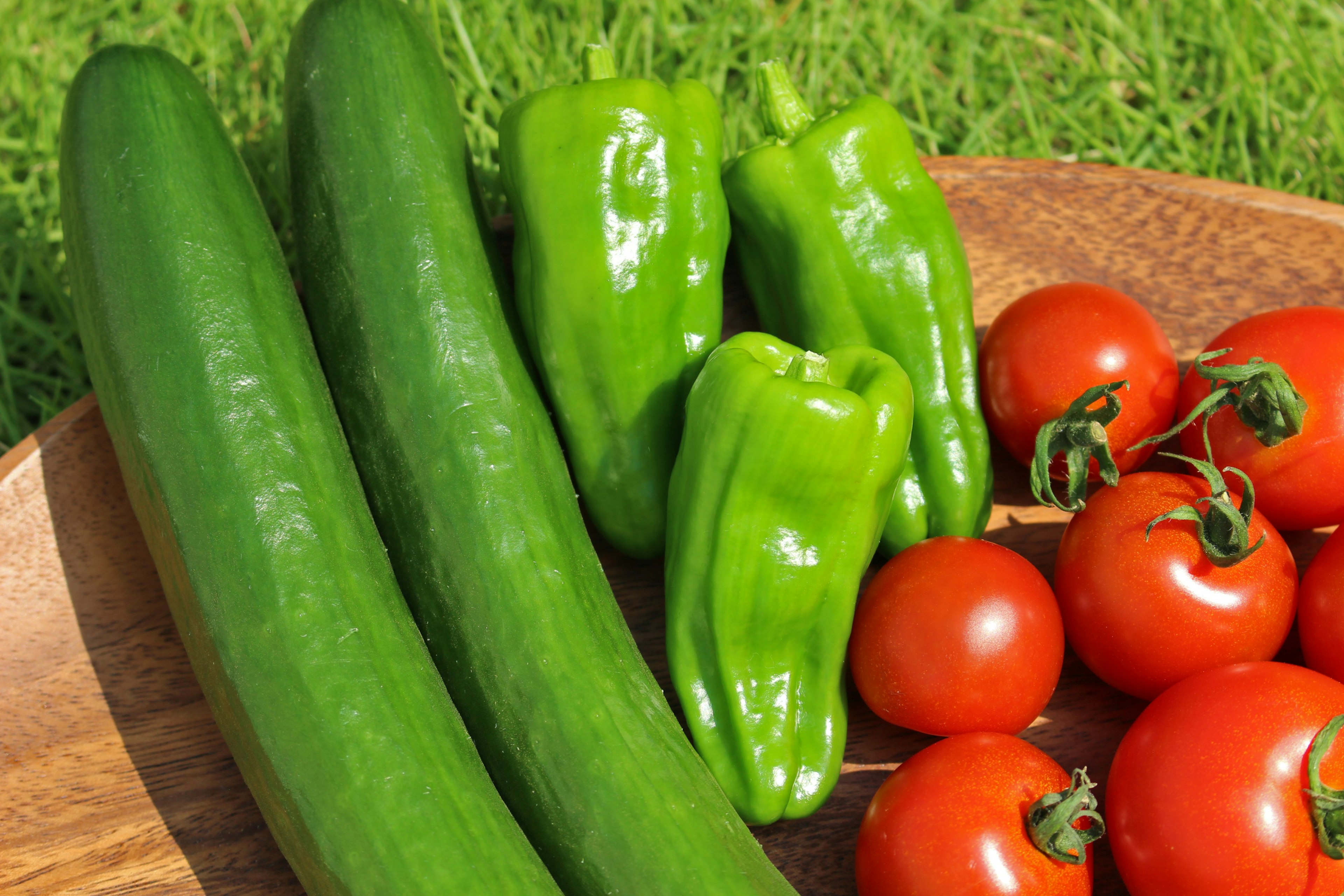 Fresh green cucumbers and bell peppers with red tomatoes on a wooden plate