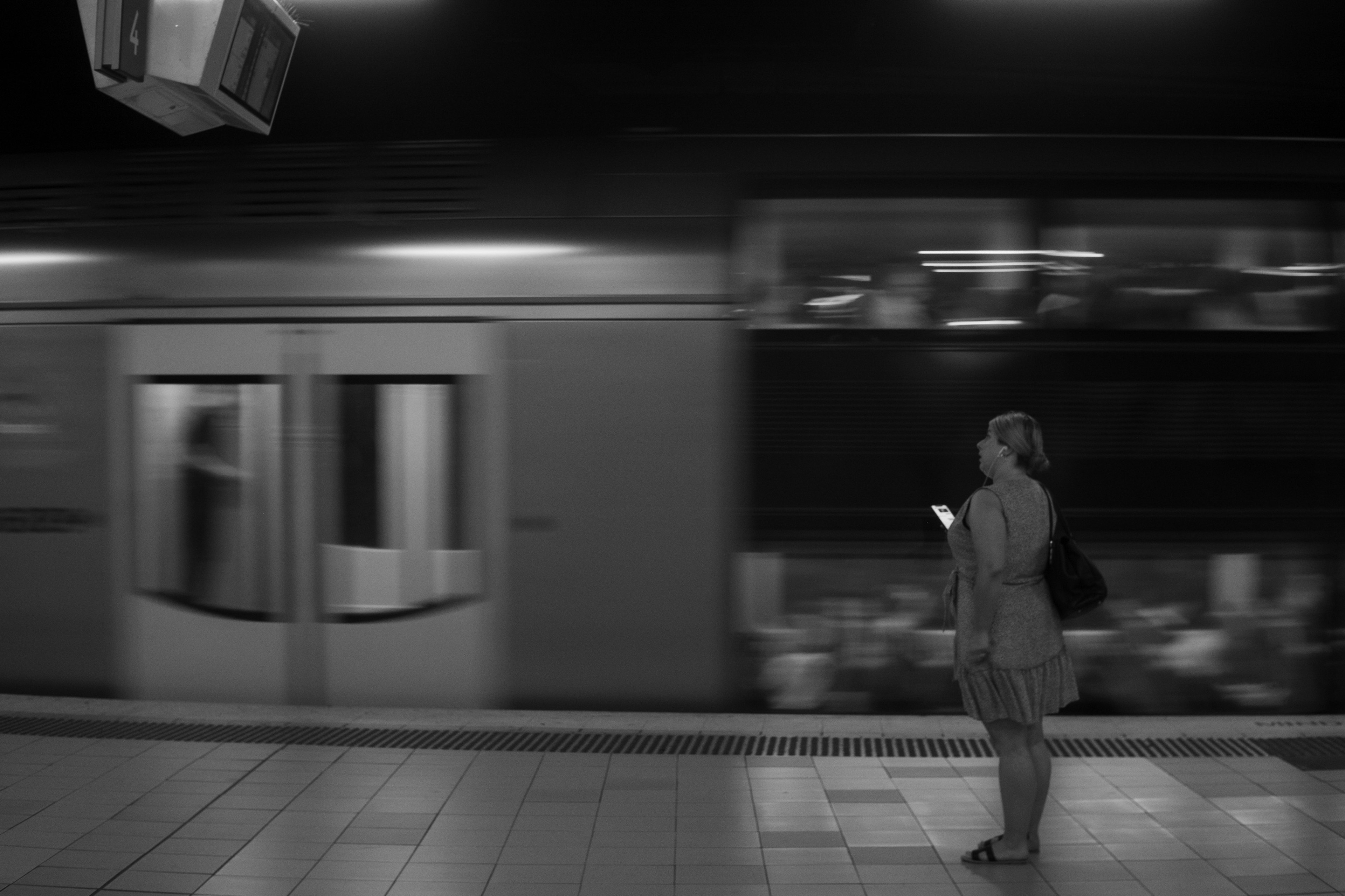 Una mujer esperando en una estación de metro en blanco y negro con un tren que pasa