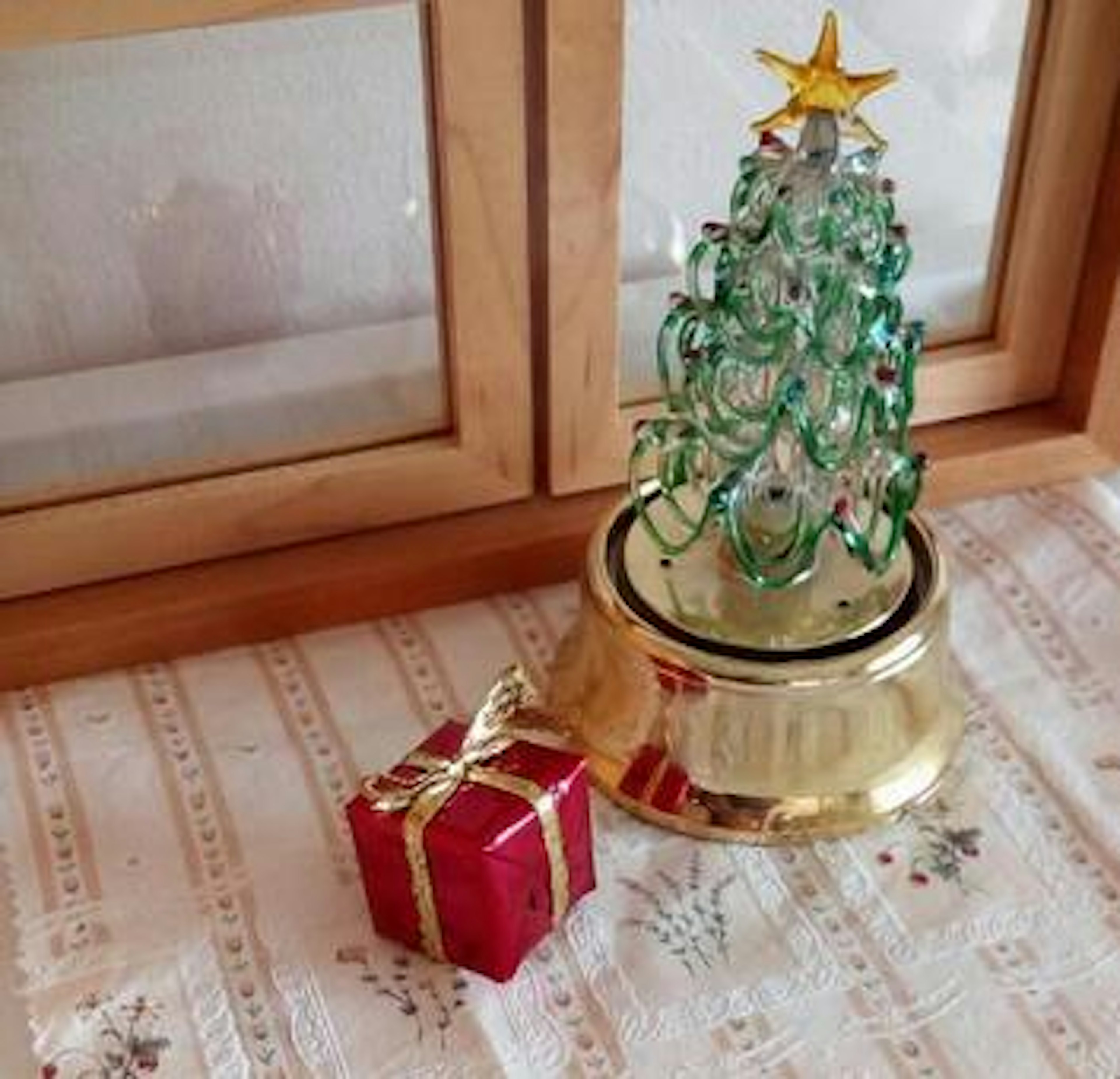 Green glass Christmas tree with a gold base and a red gift box on a decorated table