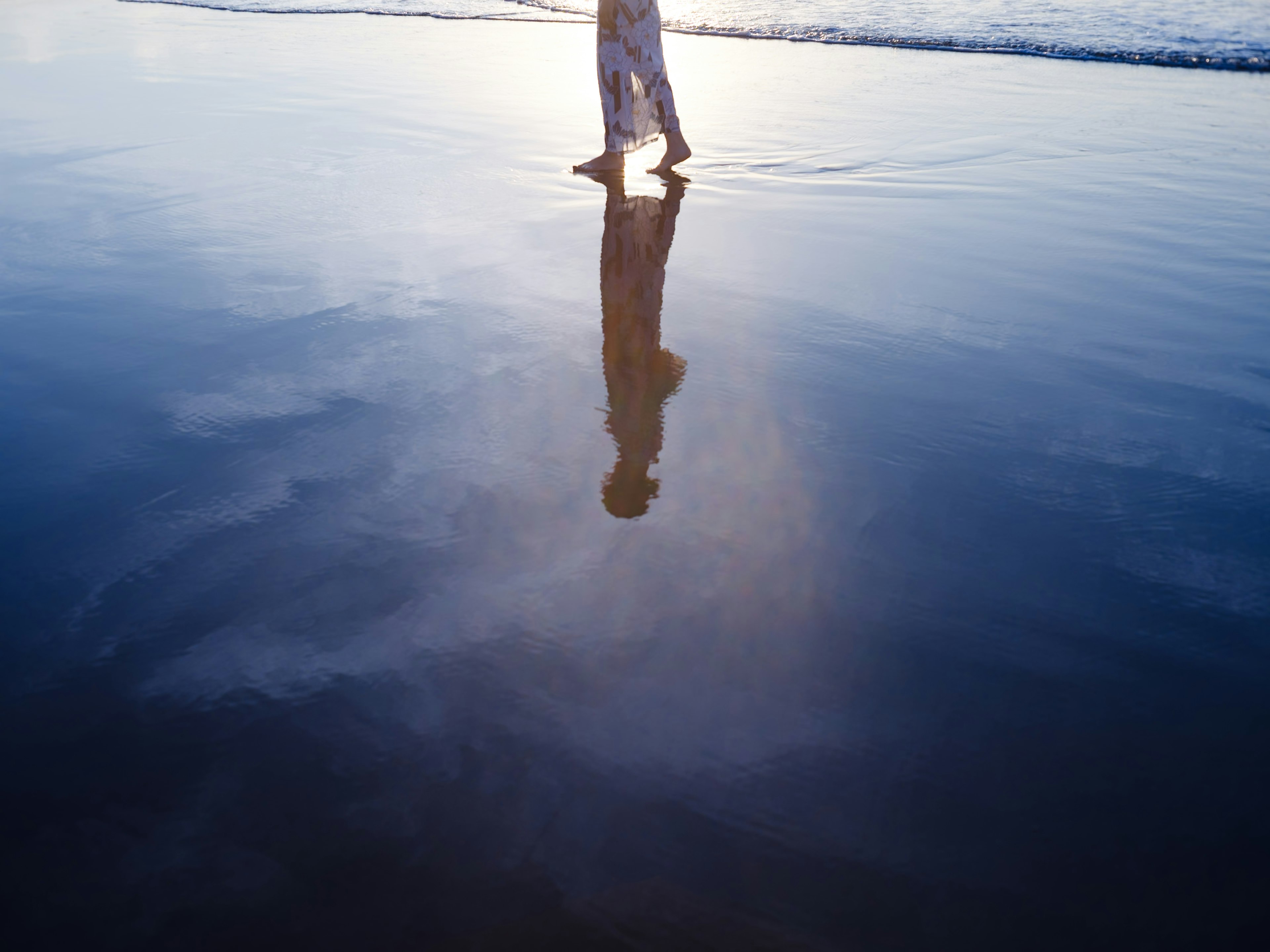 Person geht am Strand mit Reflexion im Wasser