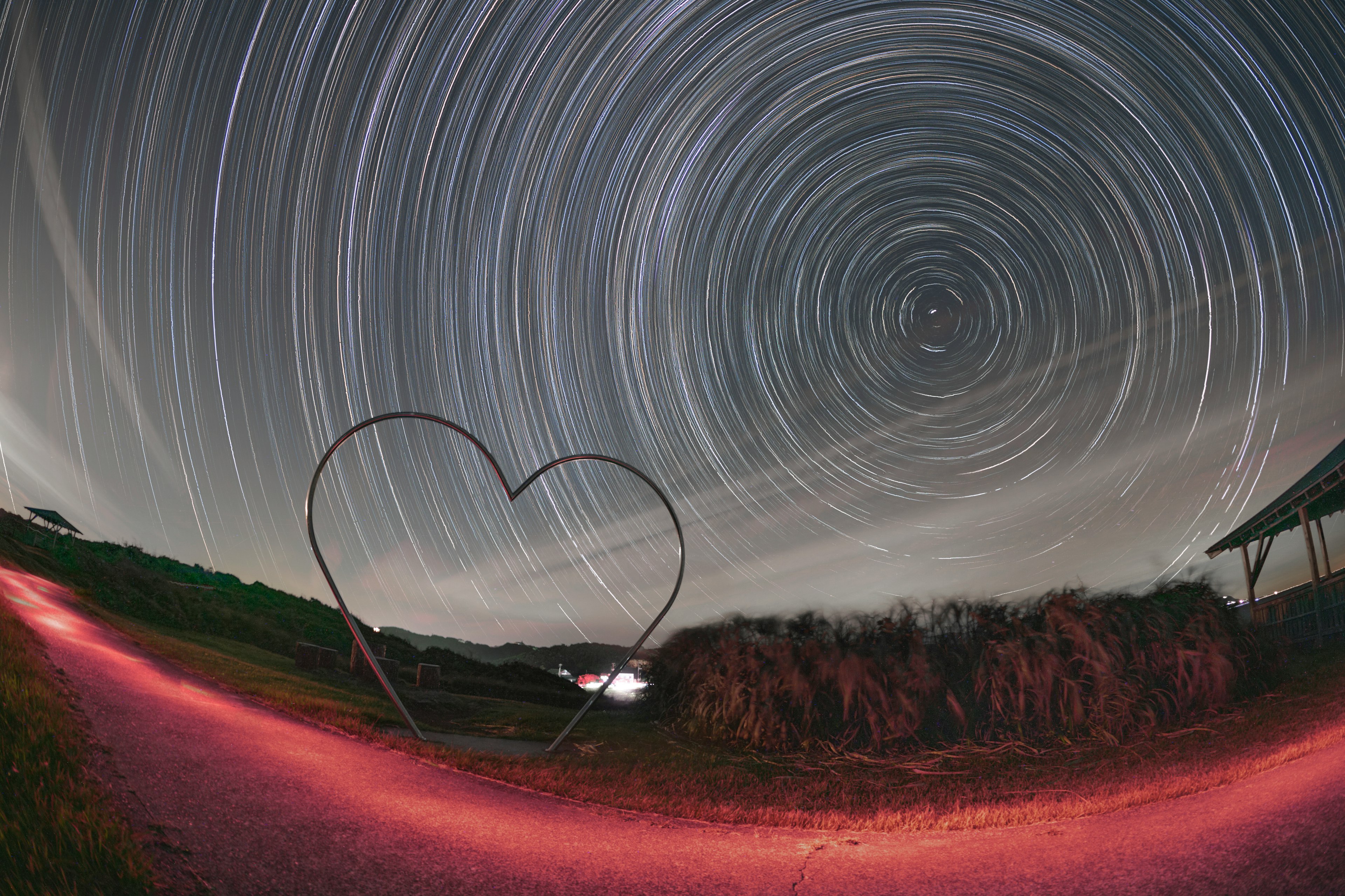 星の軌跡が描かれた夜空とハート形のオブジェがある風景