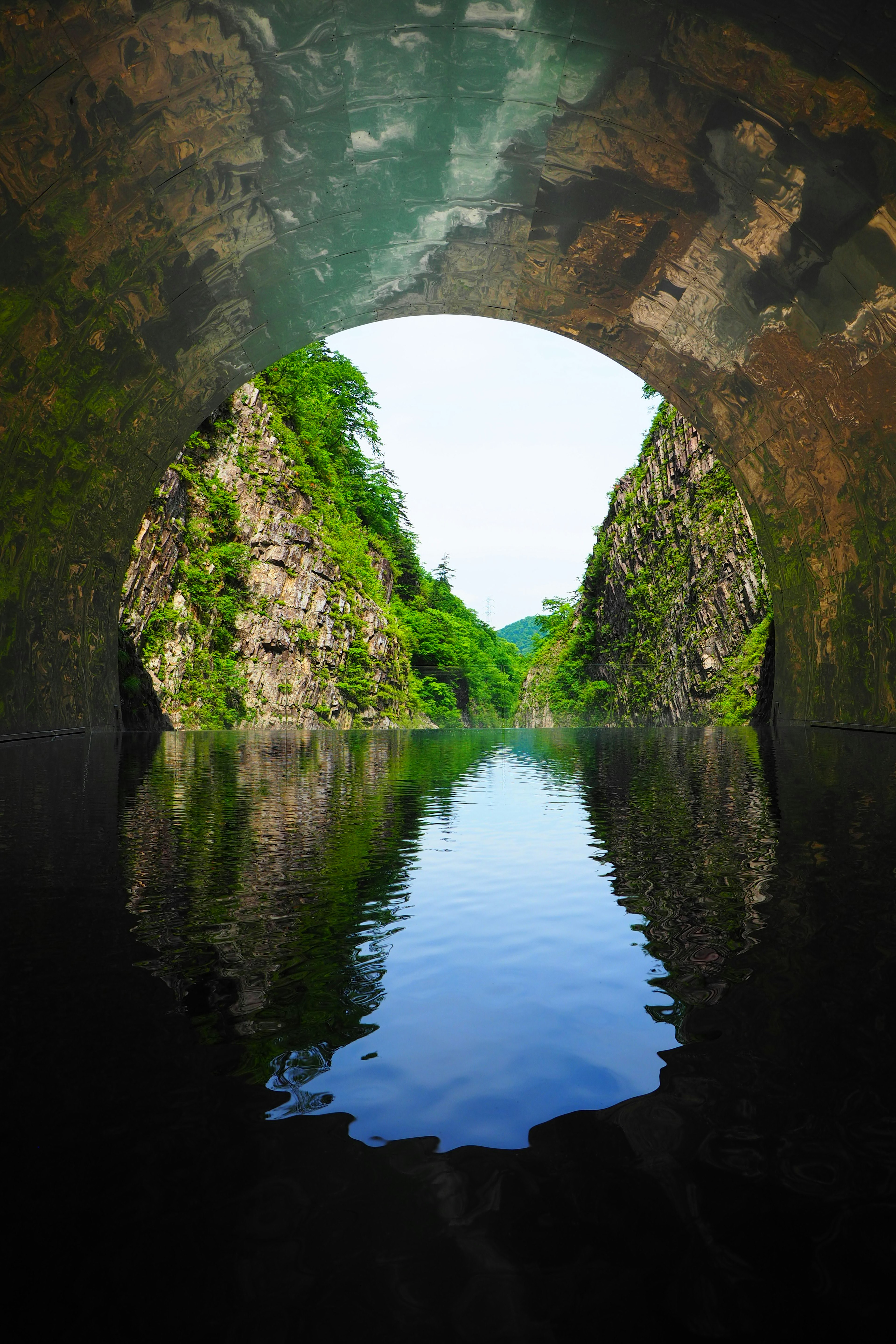 Interior view of a tunnel with lush cliffs and water reflection