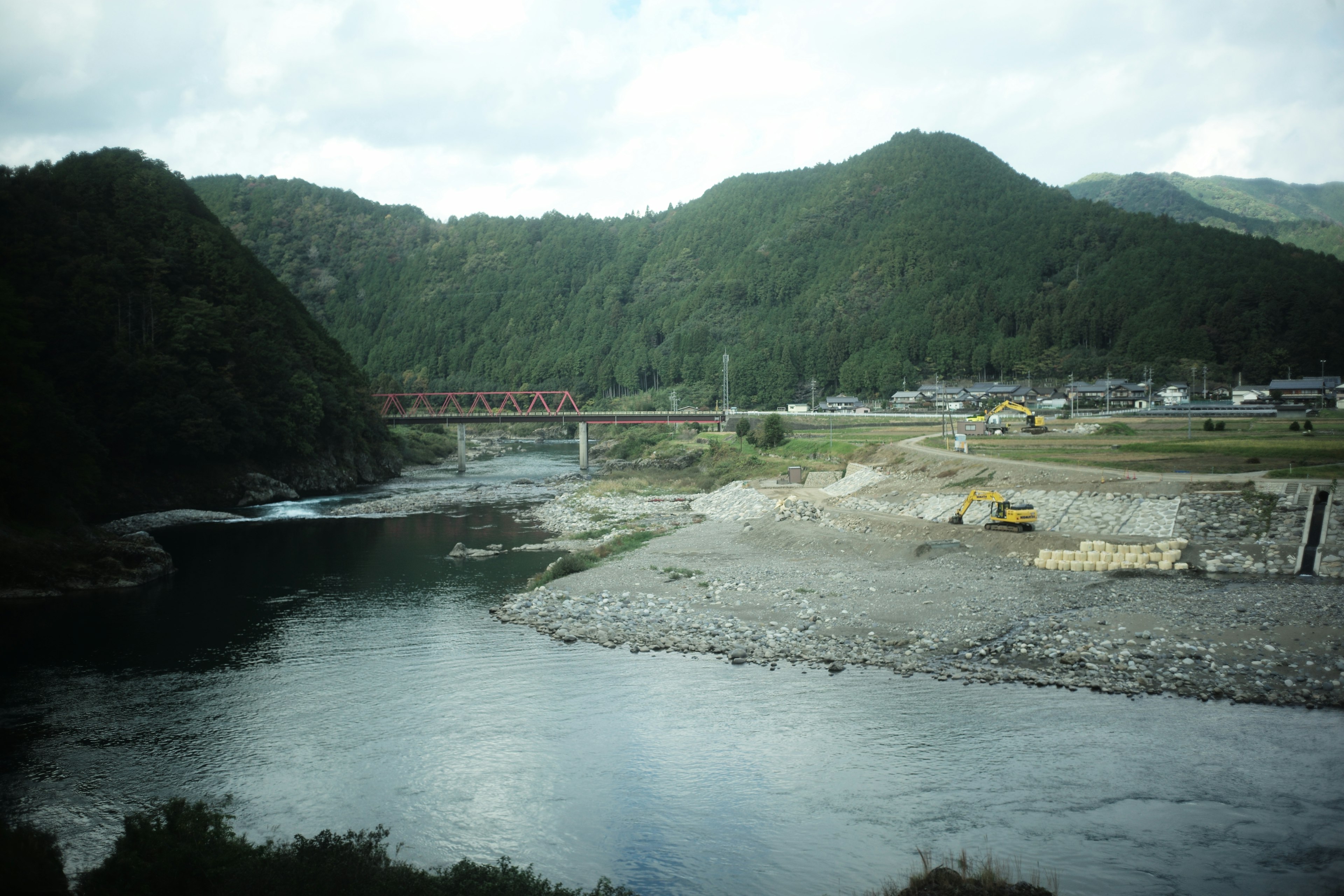 Scenic view of a river and mountains featuring a bridge and village