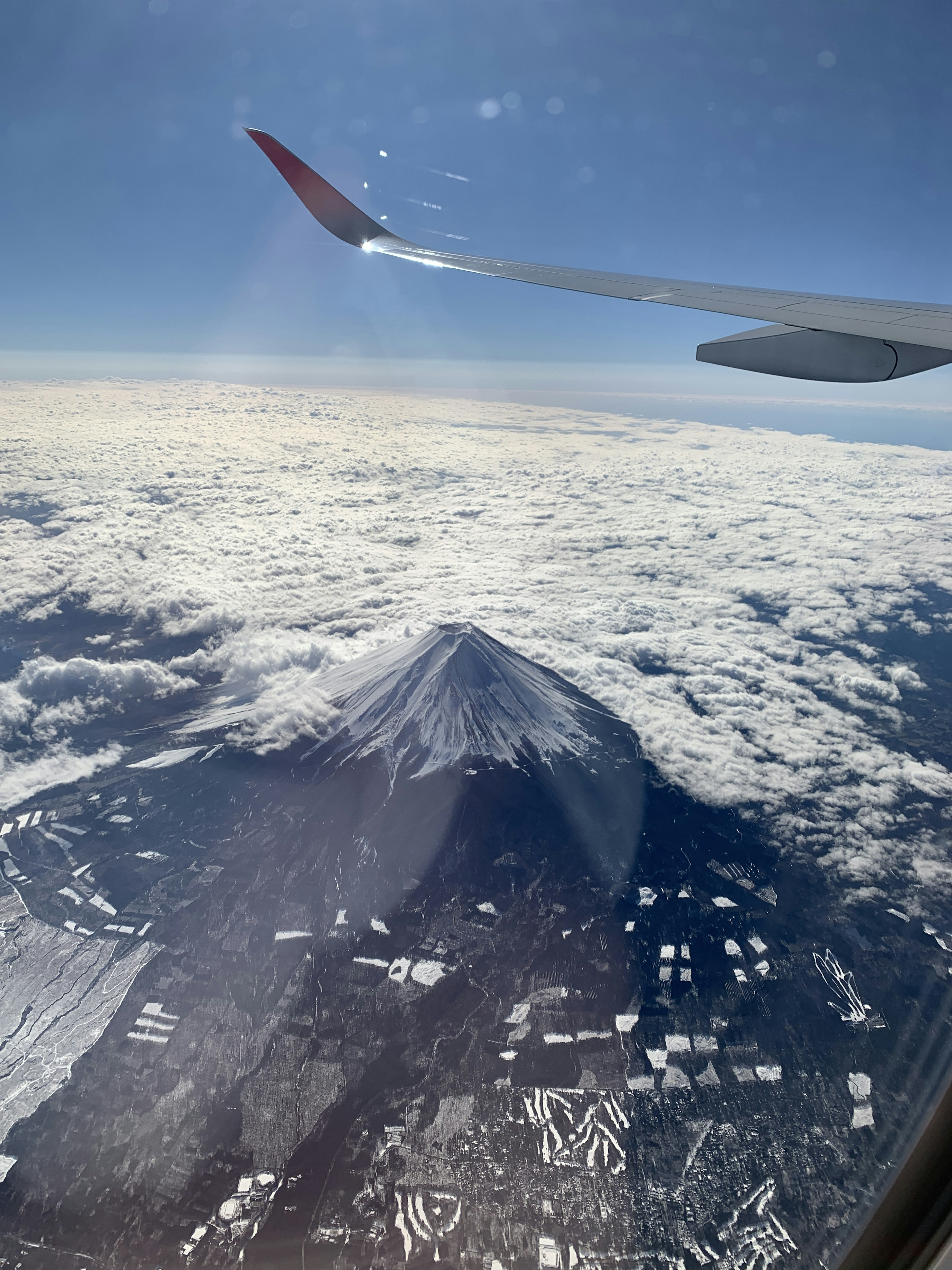 Mount Fuji rising above the clouds with an airplane wing