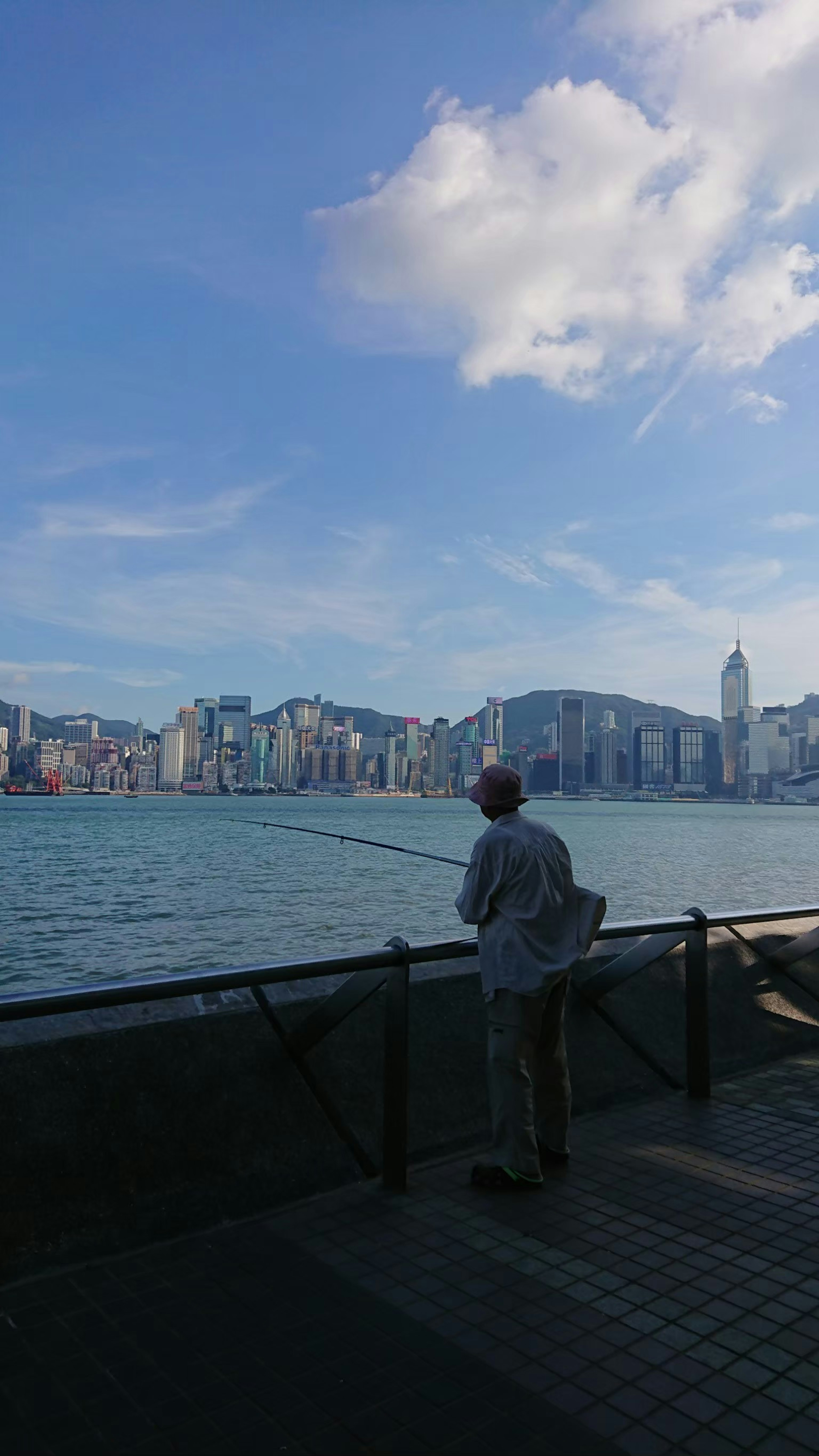 A man fishing by the waterfront with a skyline of high-rise buildings