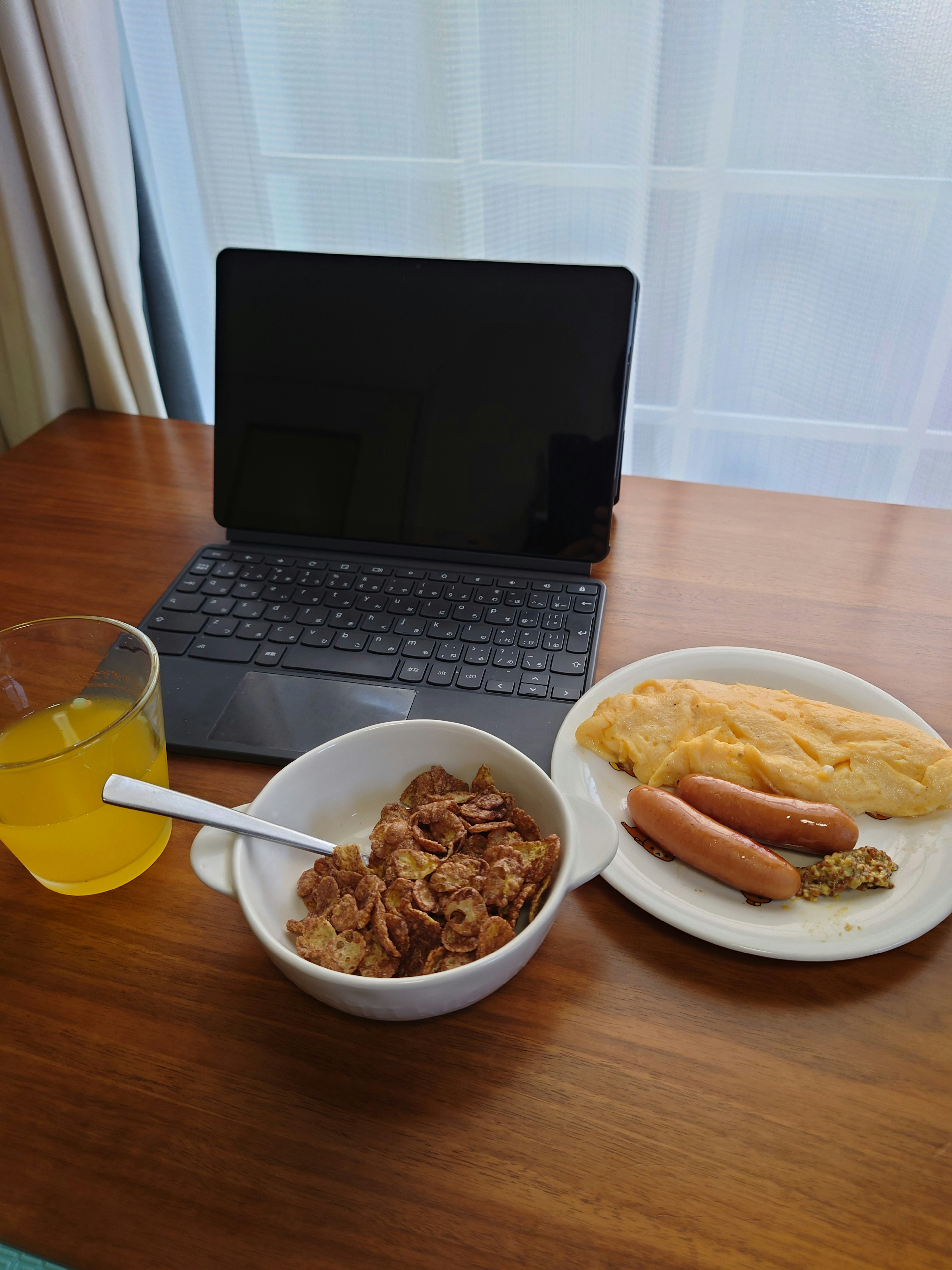 Tableta sobre una mesa de madera junto a un tazón de cerdo y salchichas con una tortilla y un vaso de jugo de naranja