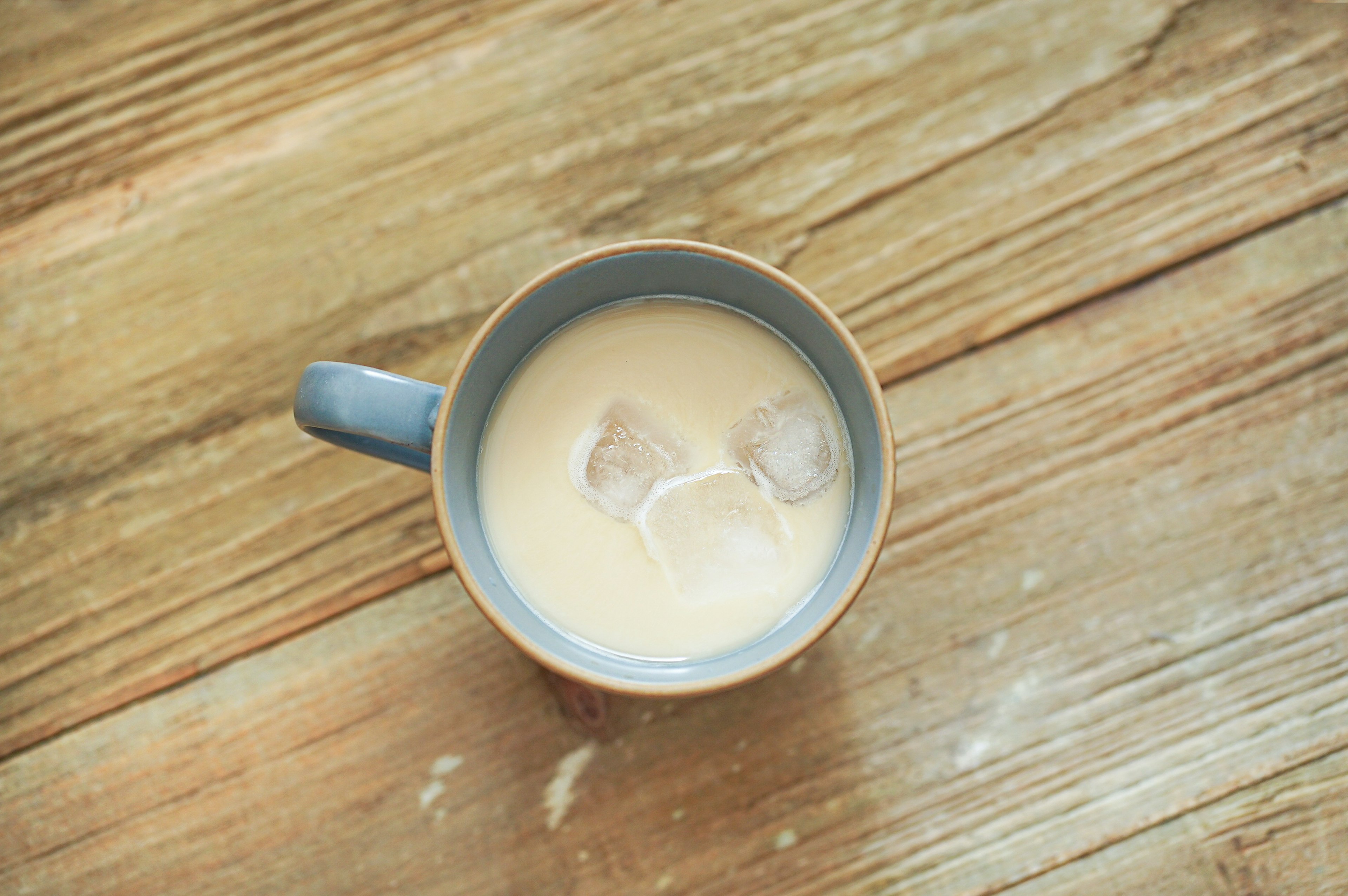 Leche con cubitos de hielo en una taza azul sobre una mesa de madera