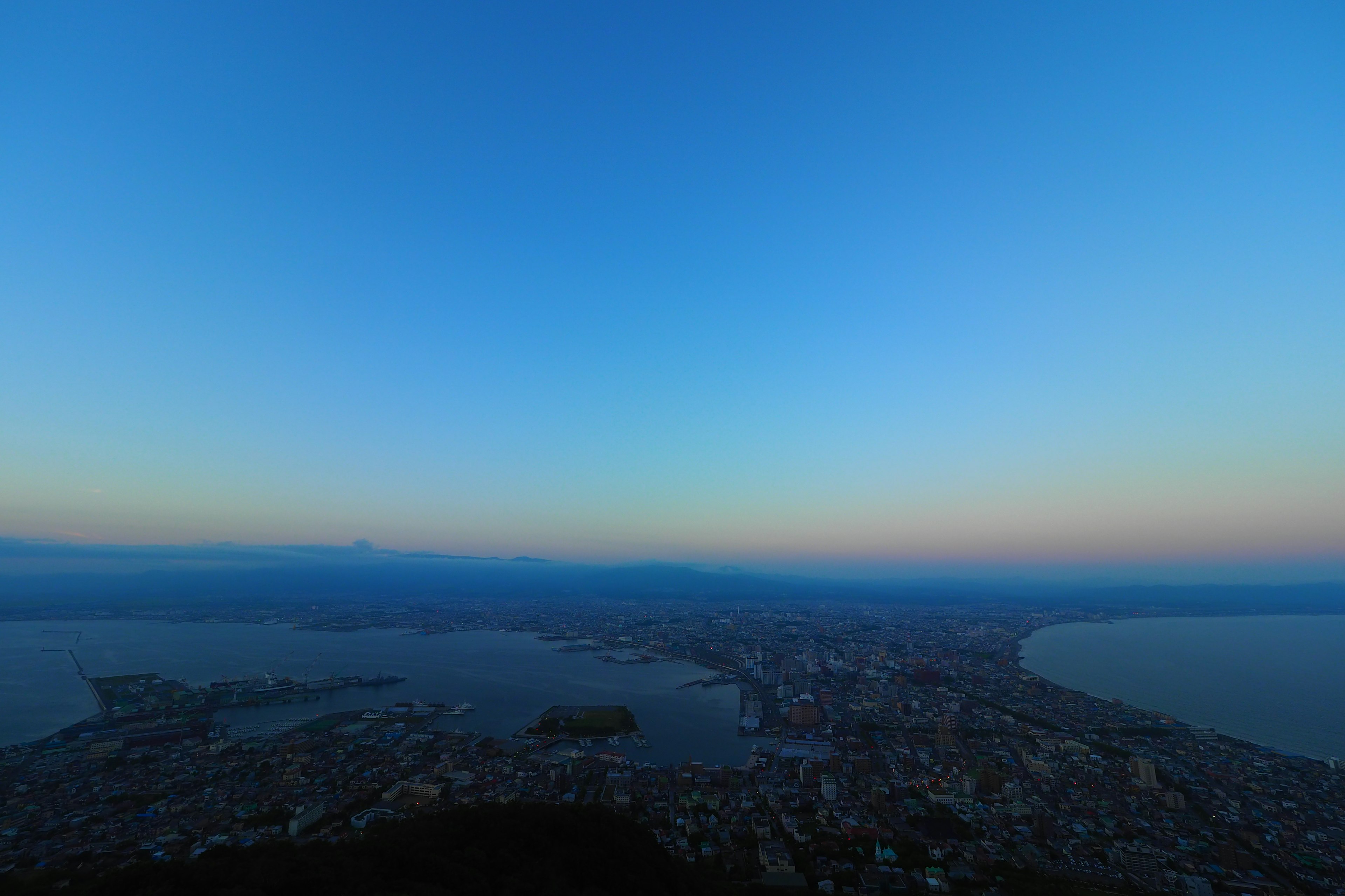 Pemandangan panorama kota dikelilingi langit biru dan laut saat senja