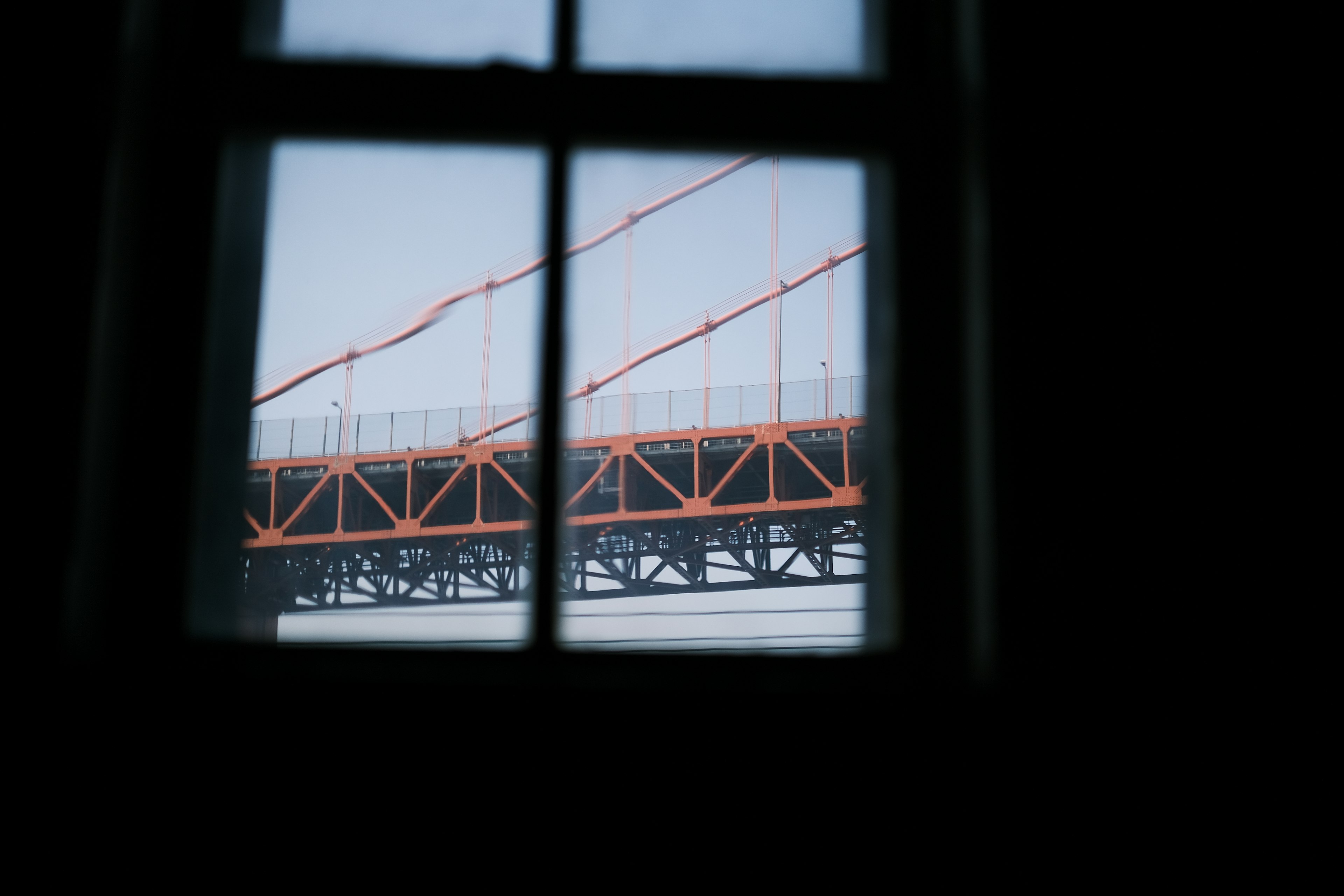 View of an orange bridge through a window with a cloudy sky