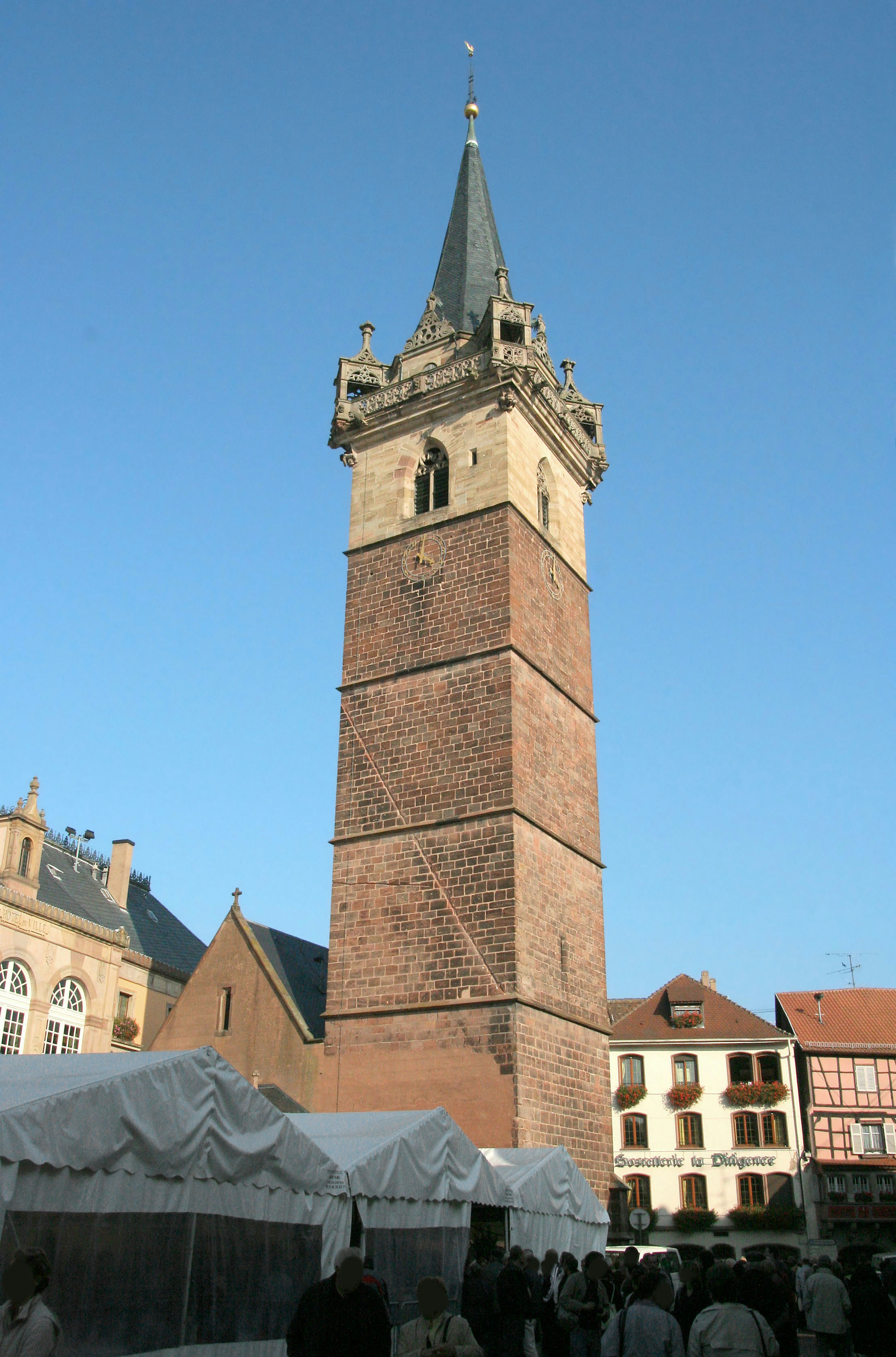 Torre del reloj de ladrillo histórico en una plaza de mercado bajo un cielo azul