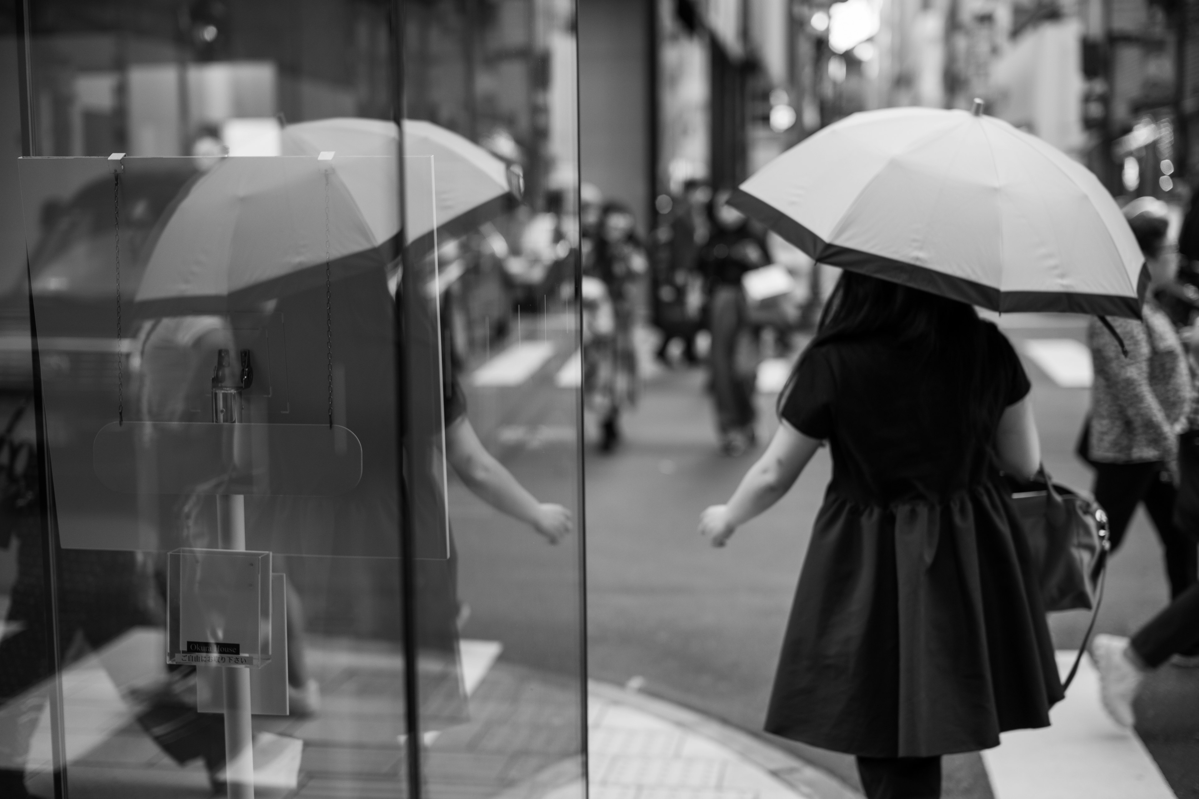 黑白照片中一位女性在街上走着，手持雨伞