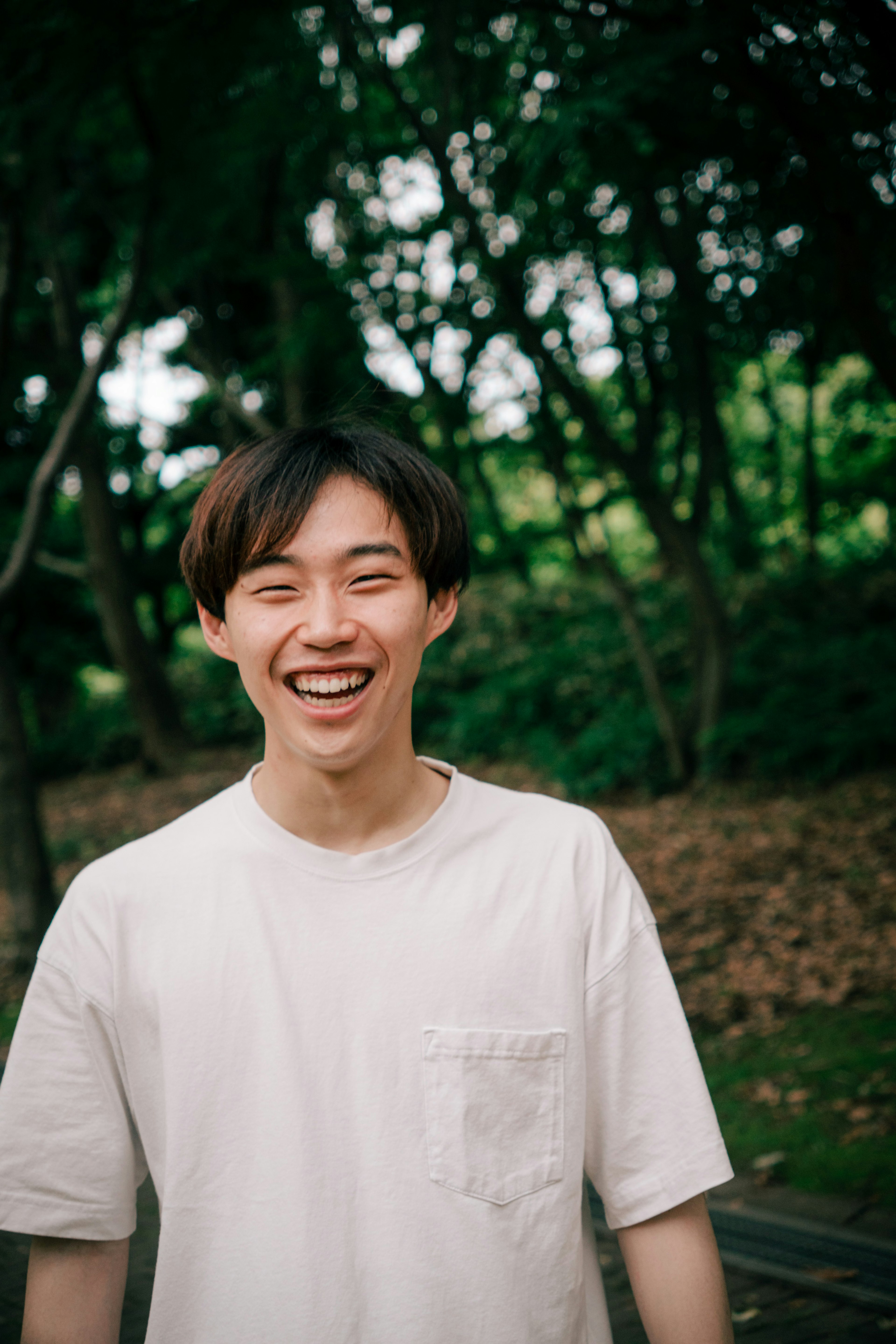 公園で笑顔の若い男性が白いTシャツを着ている