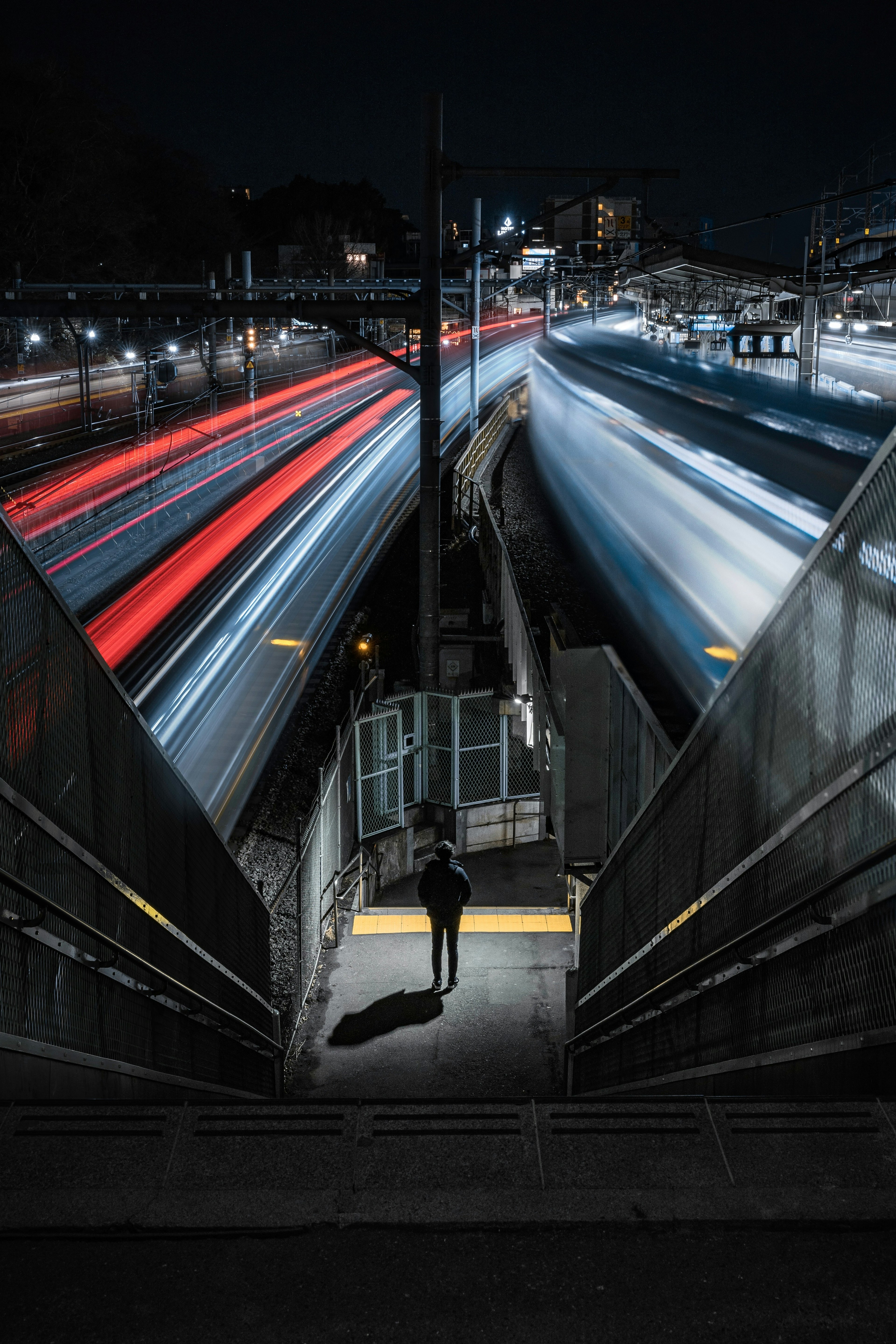 夜の街の中で光の軌跡を描く車両と階段を下る人物