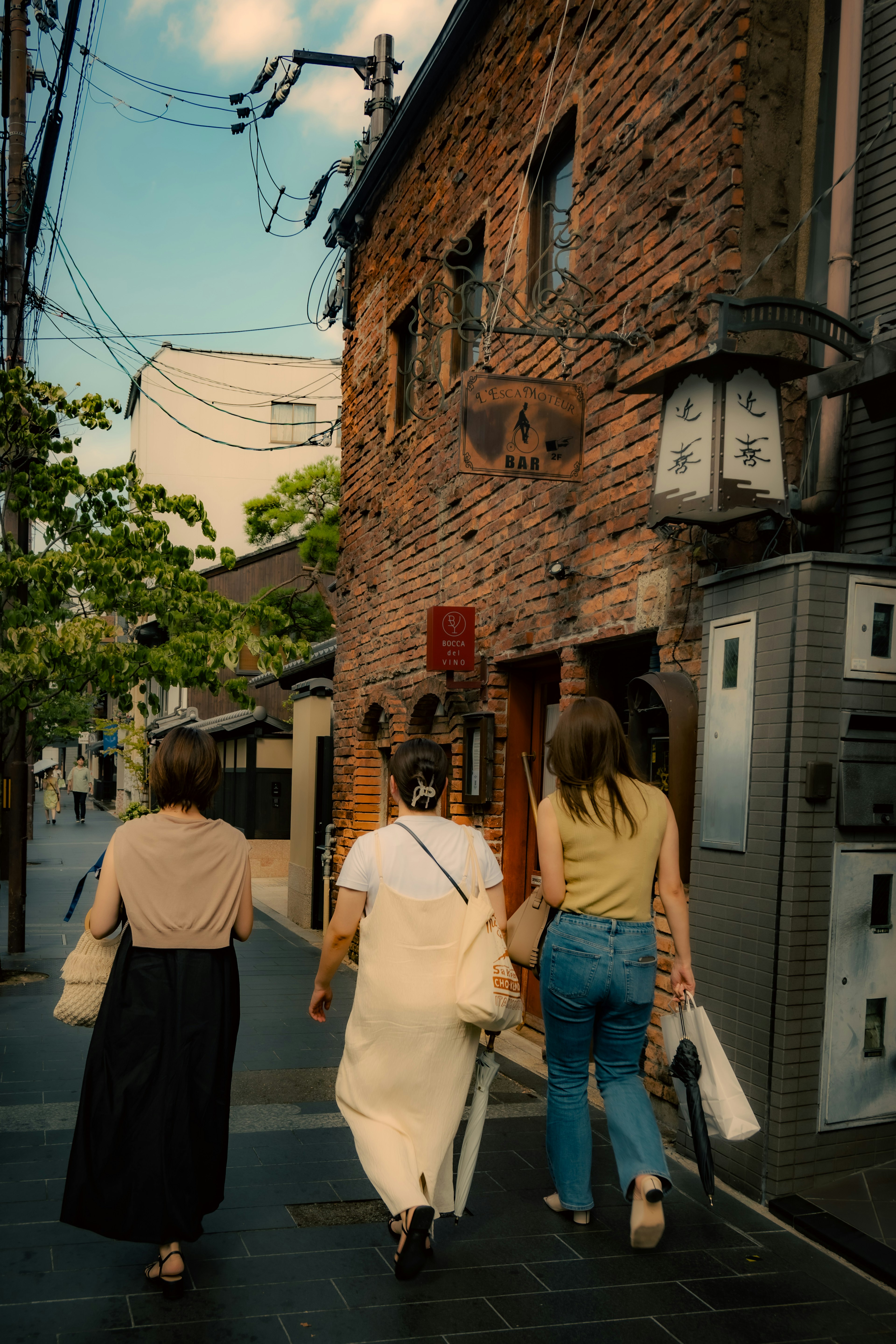 古いレンガの建物の前を歩く三人の女性の後ろ姿