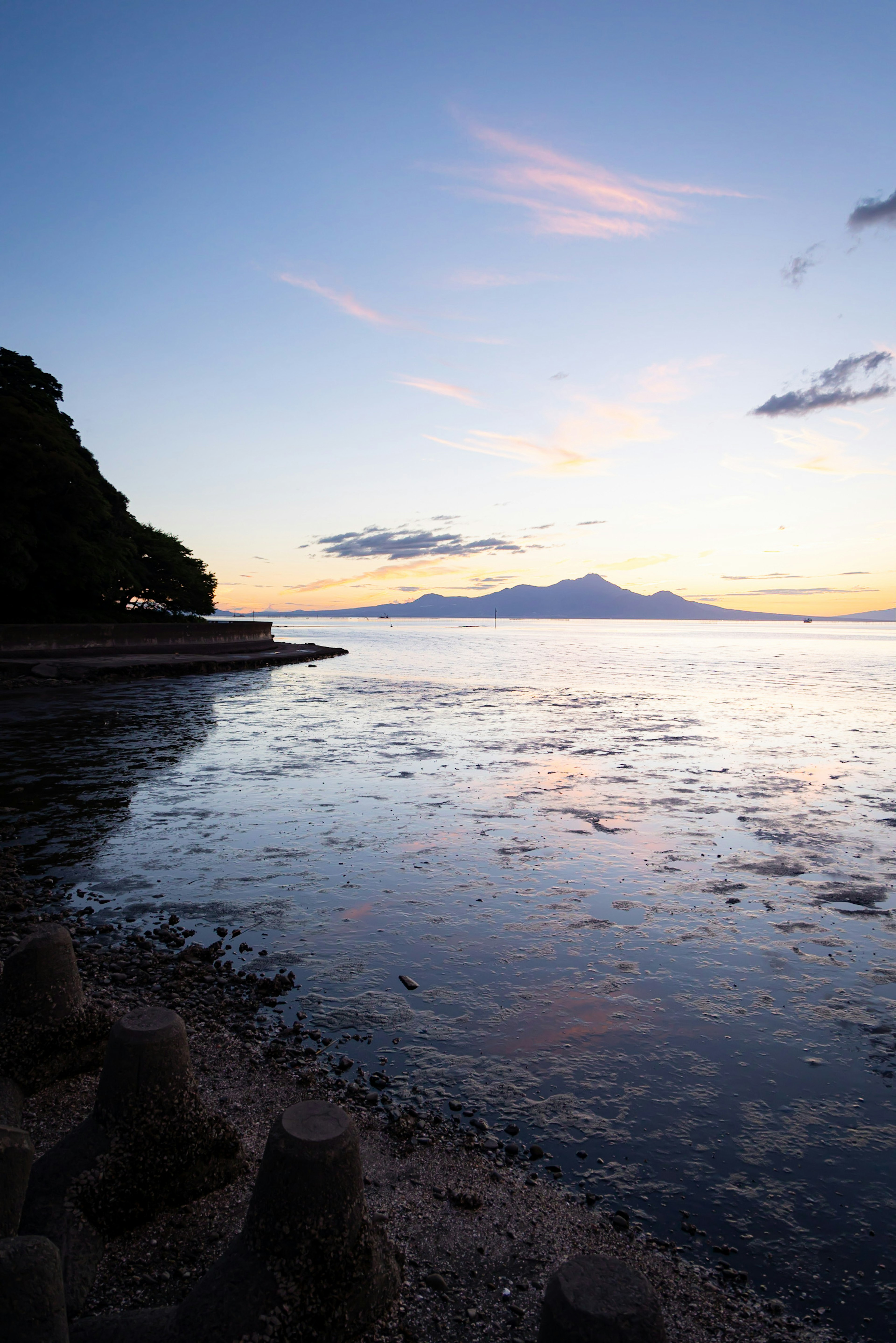 静かな海の景色と山のシルエットが広がる夕暮れの風景