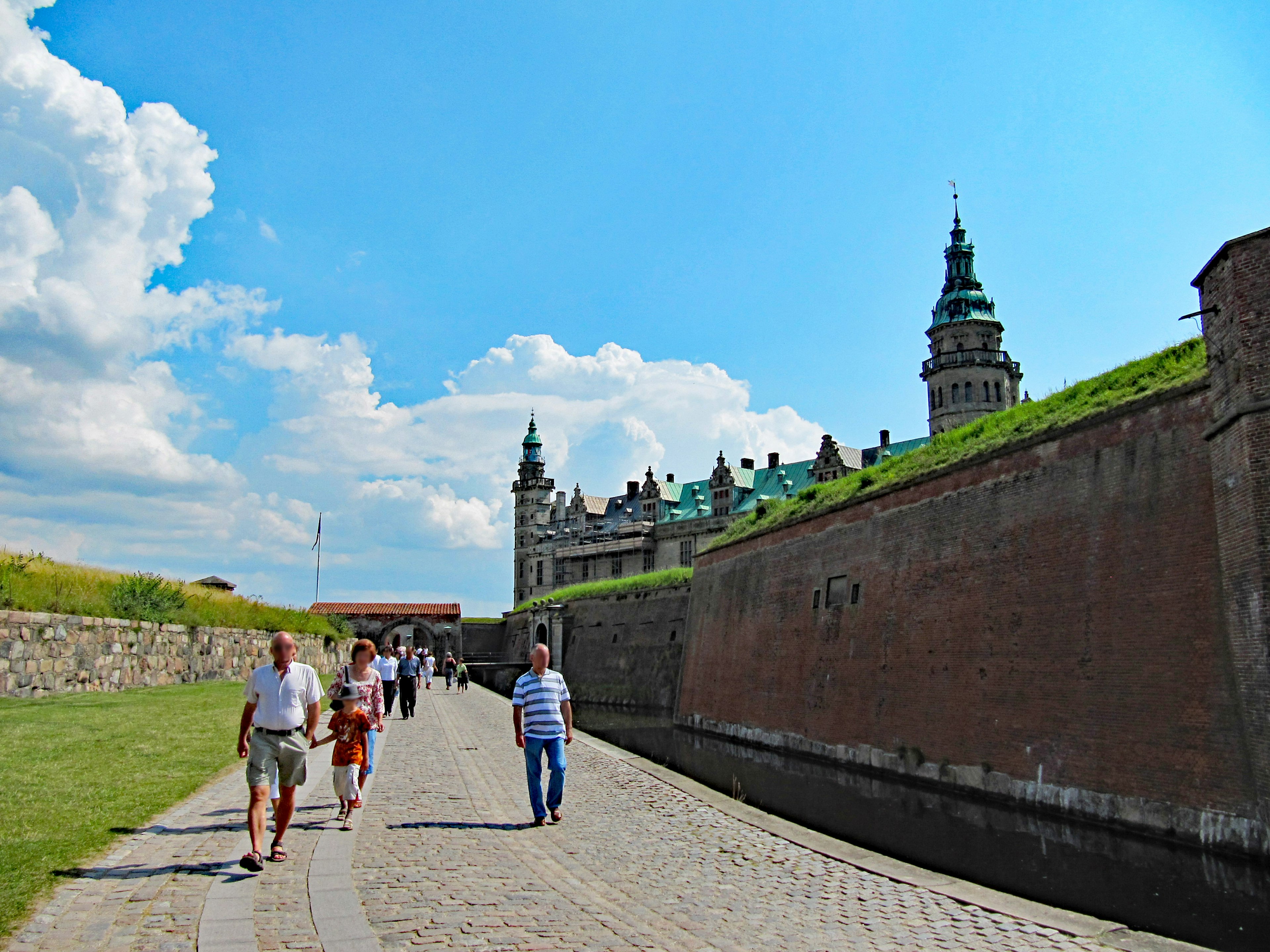 Menschen, die auf dem Weg am Schloss Kronborg entlang gehen, unter einem strahlend blauen Himmel