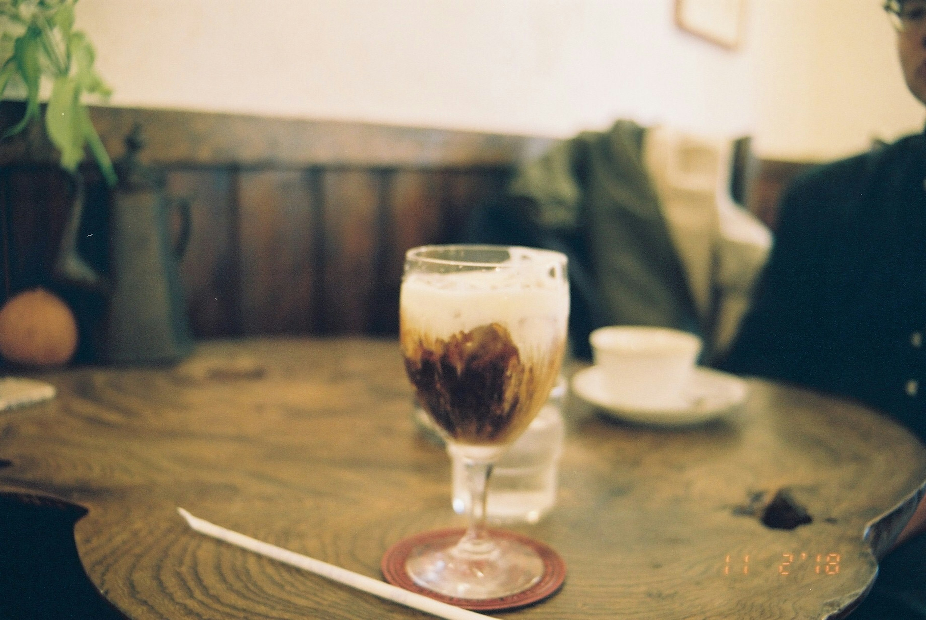 Gelas kopi es di atas meja kayu dengan suasana kafe yang nyaman