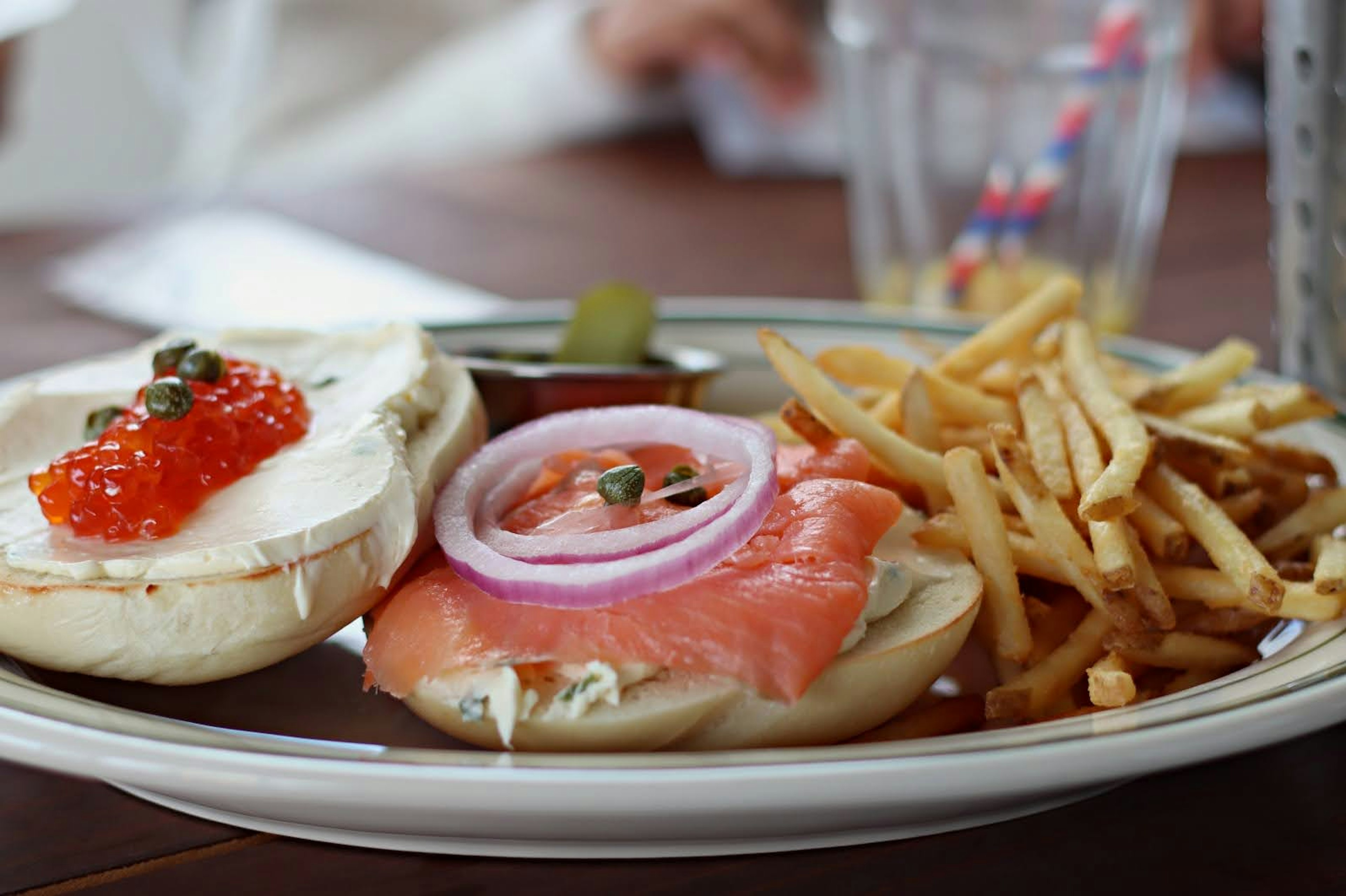 Piring bagel dengan salmon asap dan krim keju dihiasi dengan bawang merah dan kaviar disertai kentang goreng