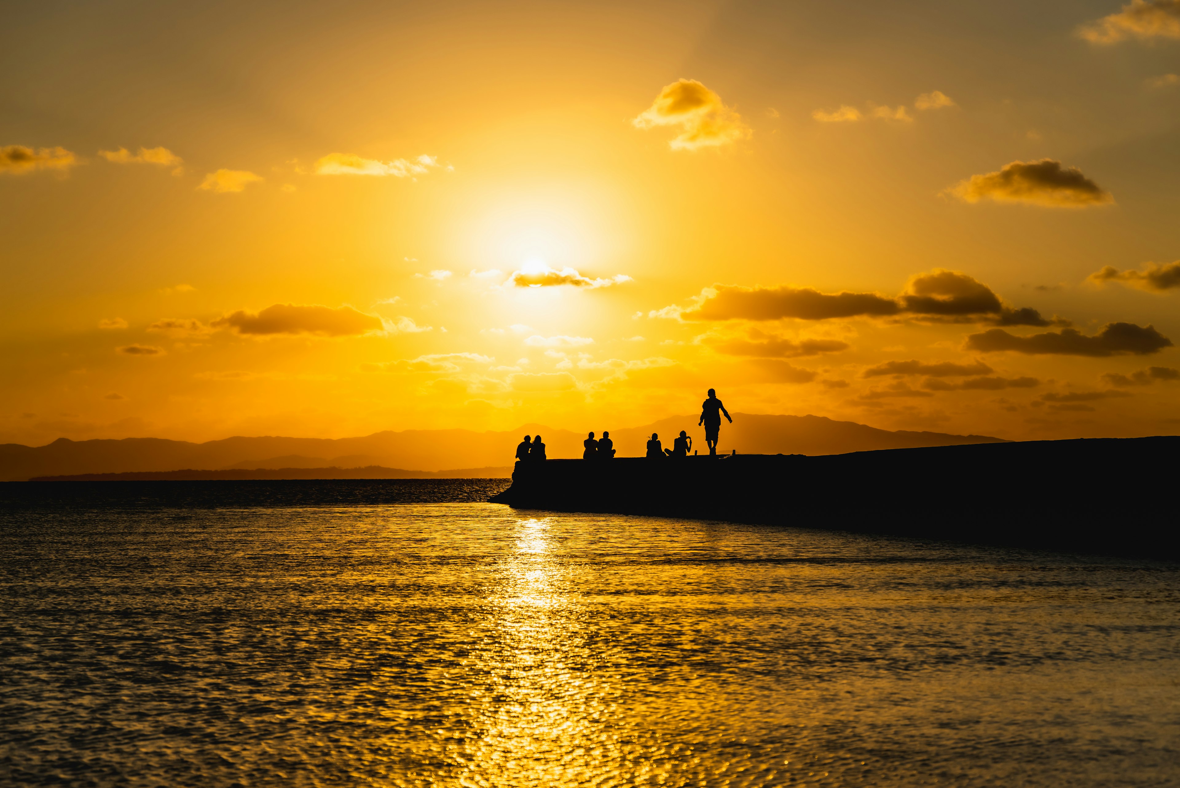 夕日が沈む海岸でシルエットの人々が立っている風景