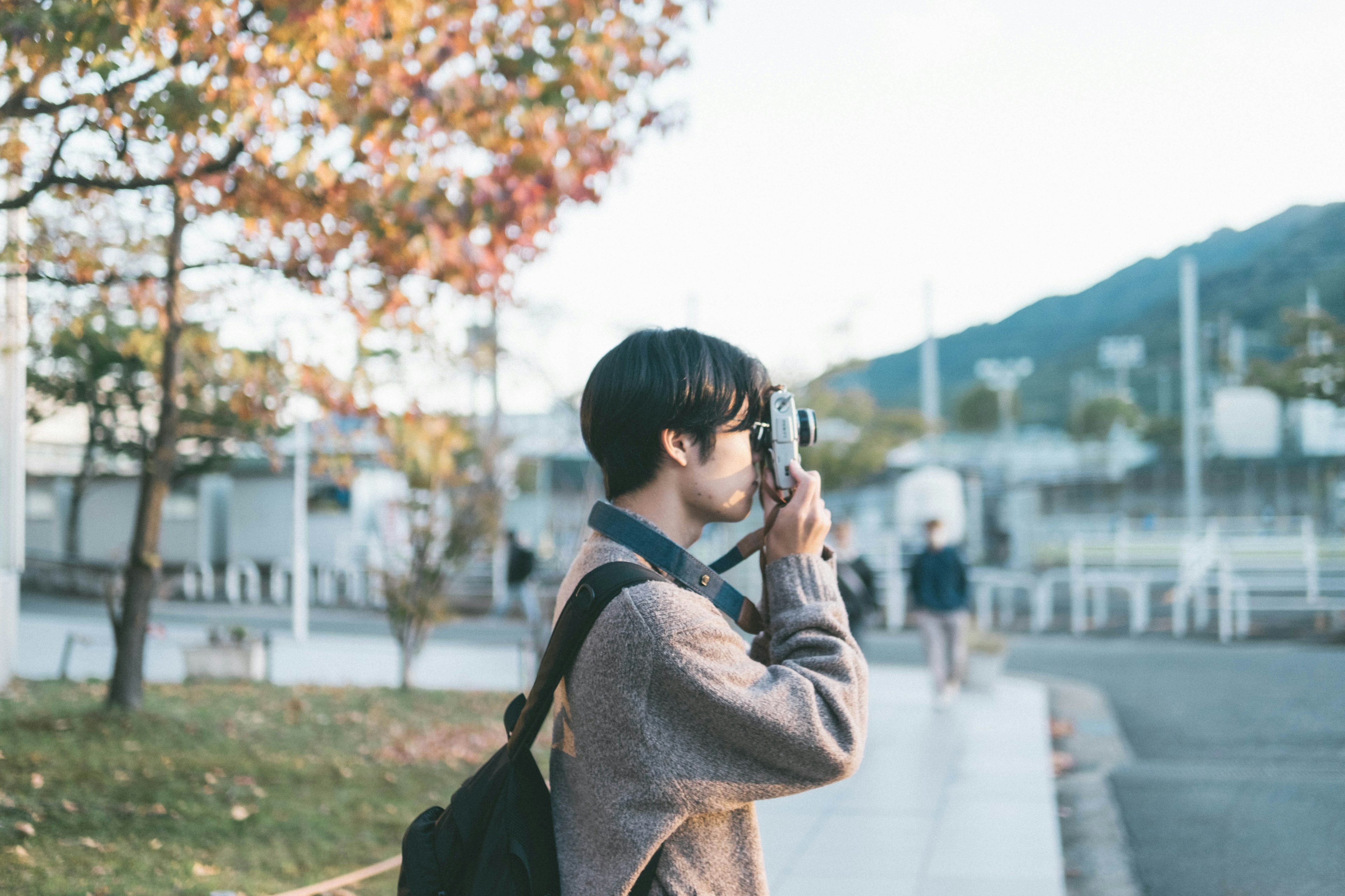 公園でカメラを持っている若い男性　秋の紅葉が背景にある