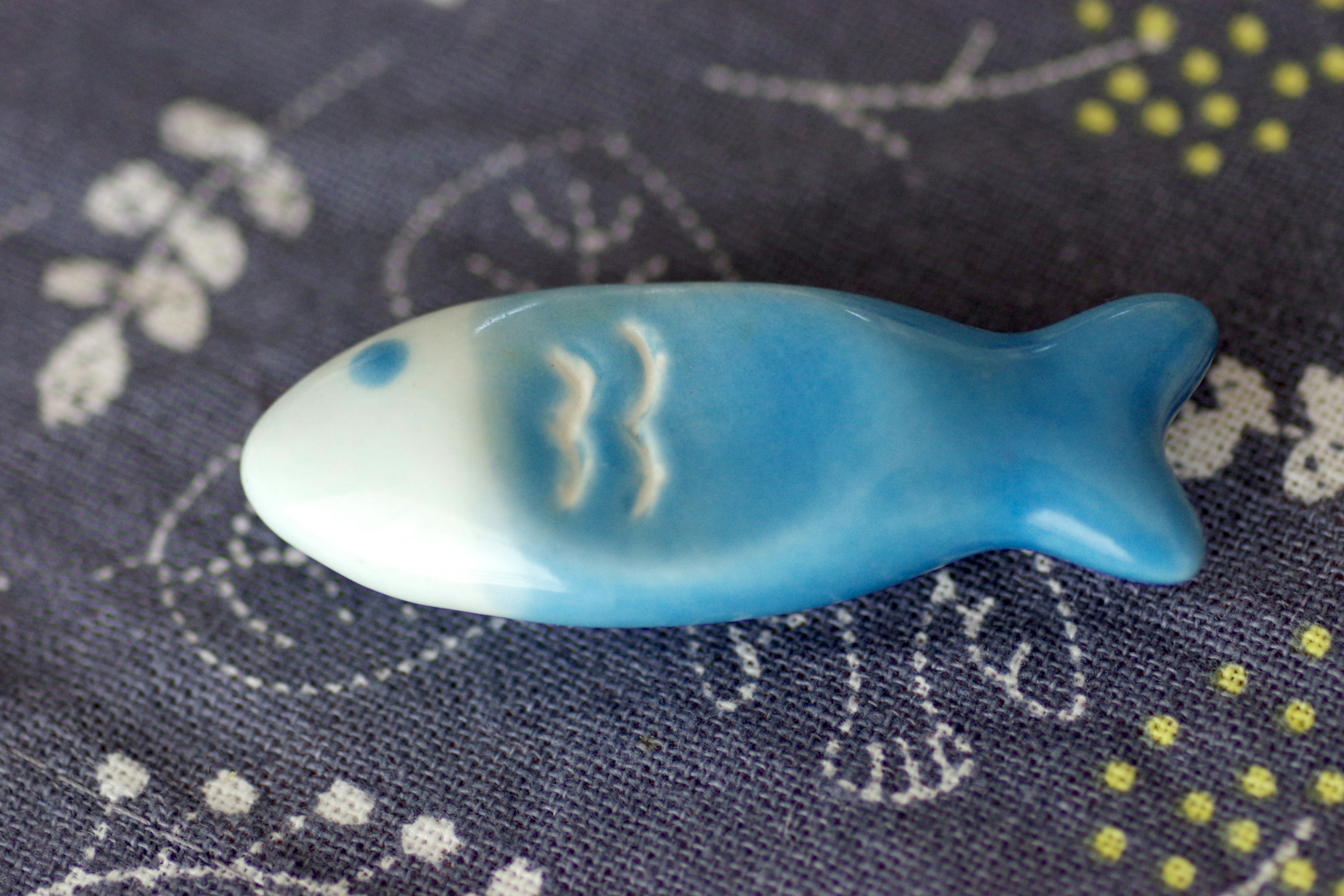 A blue fish-shaped ceramic object placed on floral fabric