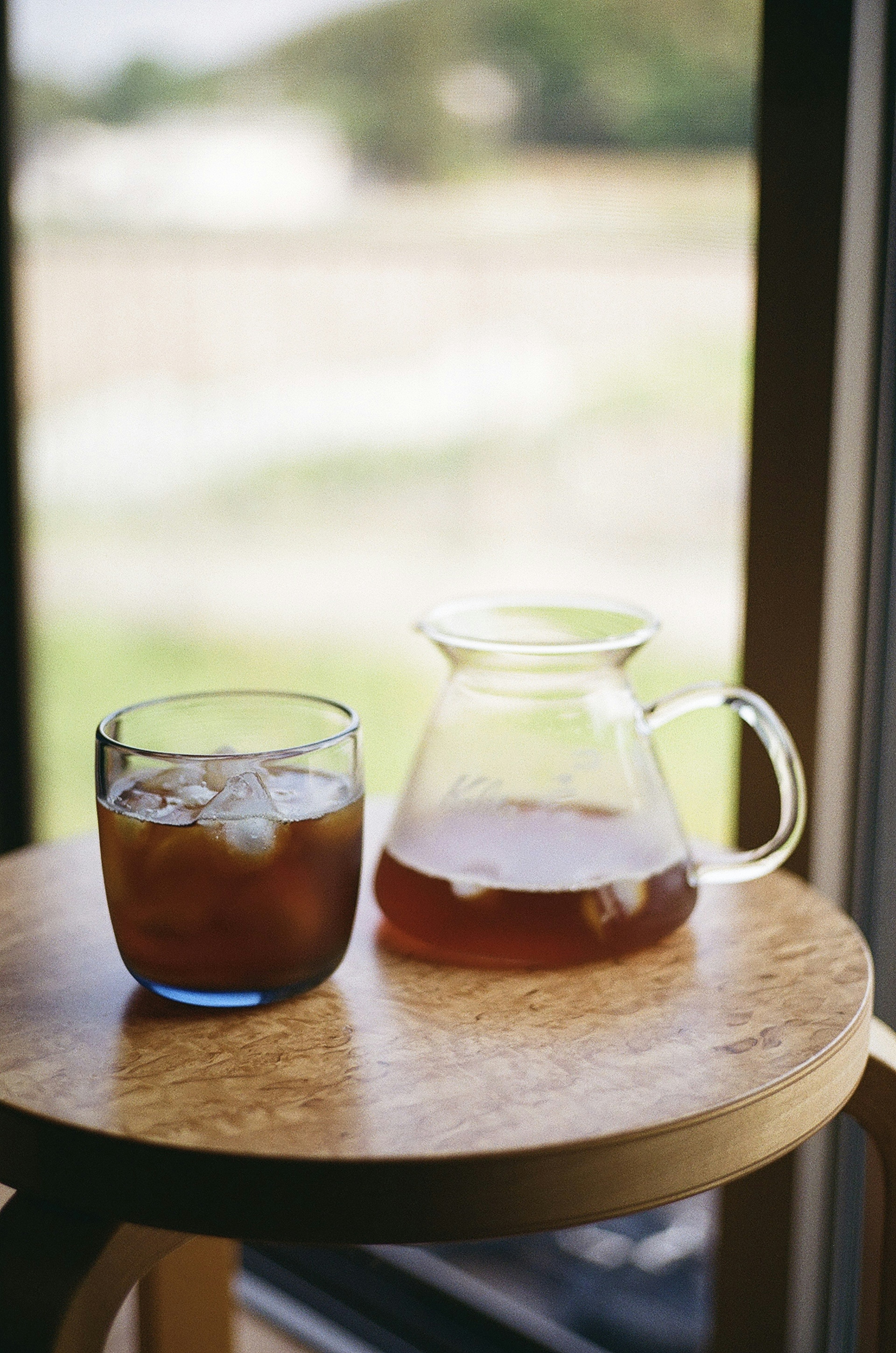 Un verre et une carafe de thé glacé sur une table en bois près de la fenêtre