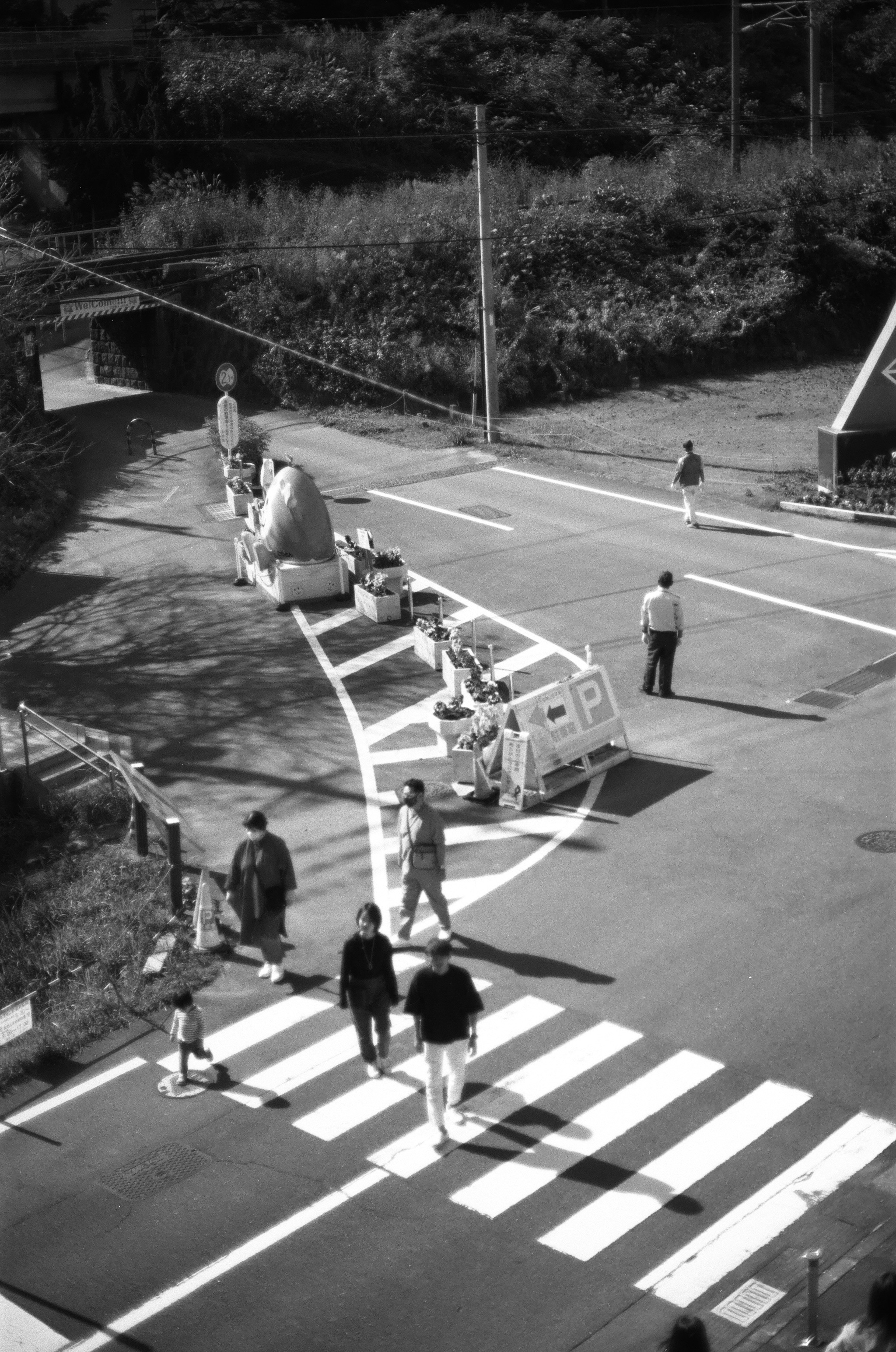 Schwarzweißfoto von Fußgängern, die eine Straße mit einem Zebrastreifen überqueren, Baustellenbarrieren und Verkehrsampel sichtbar