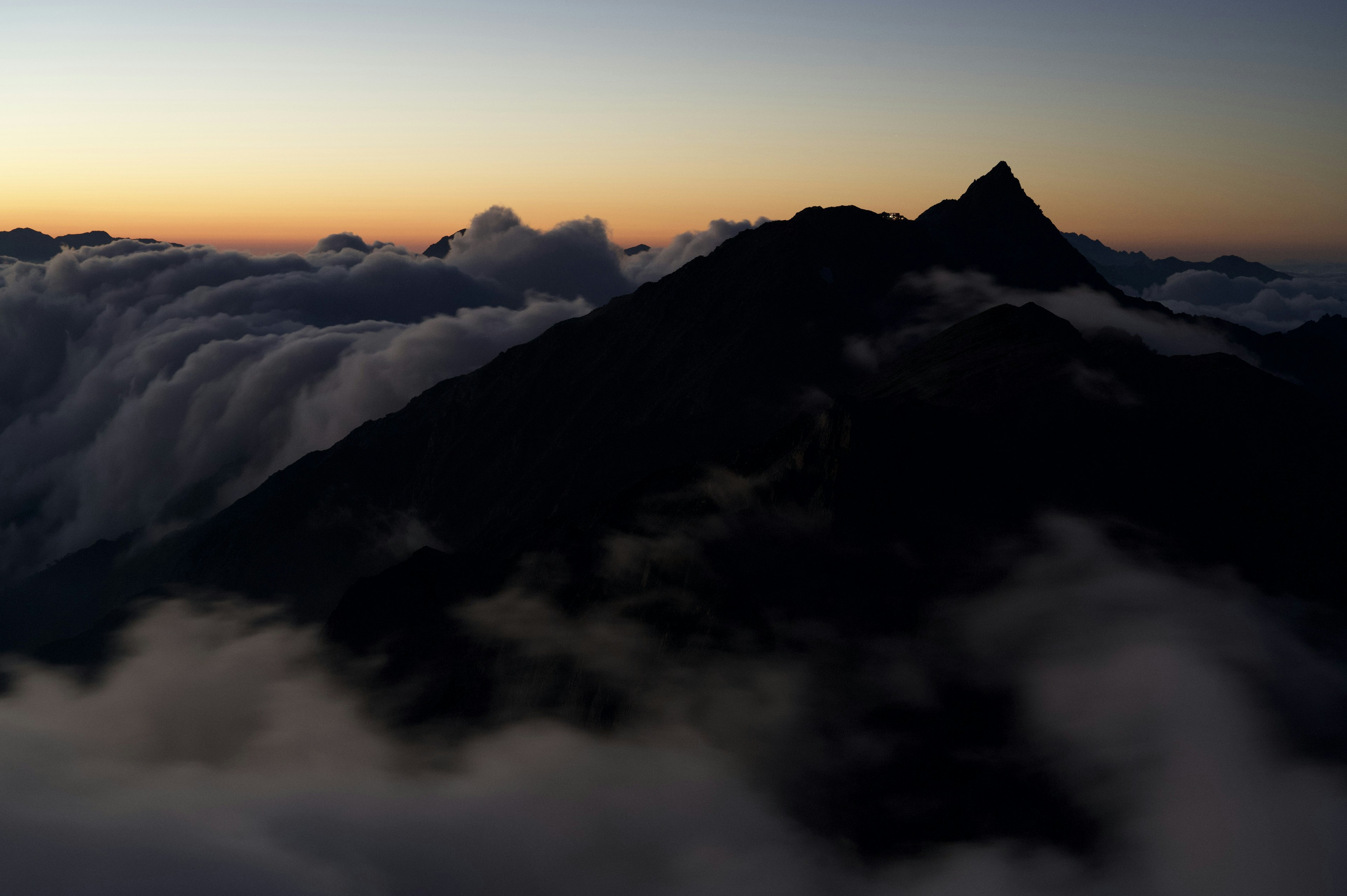 雲海の上にそびえる山のシルエットと夕暮れの空