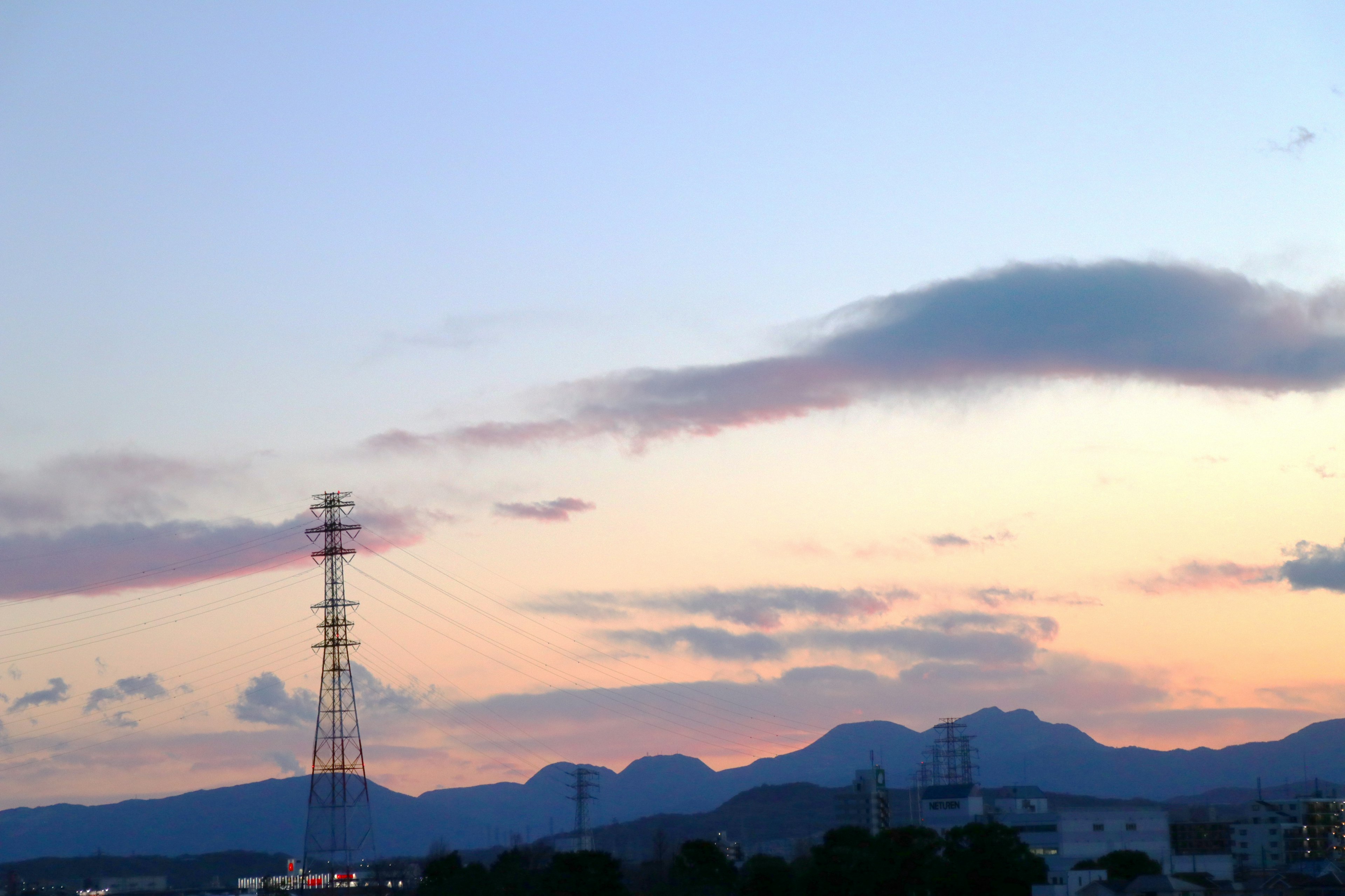 A landscape featuring a sunset sky with mountains and a power tower