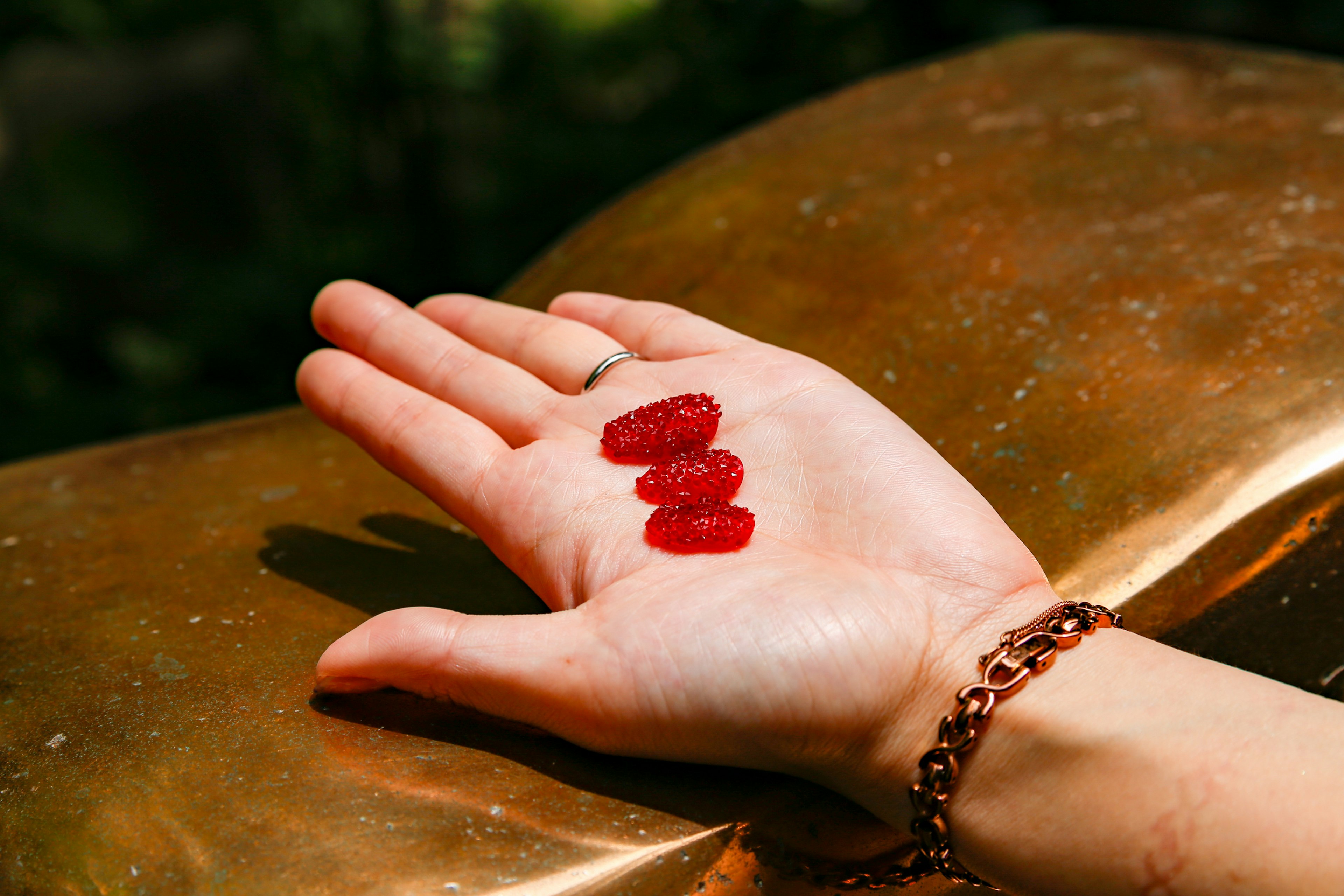 Caramelle gommose rosse appoggiate su una mano con uno sfondo dorato