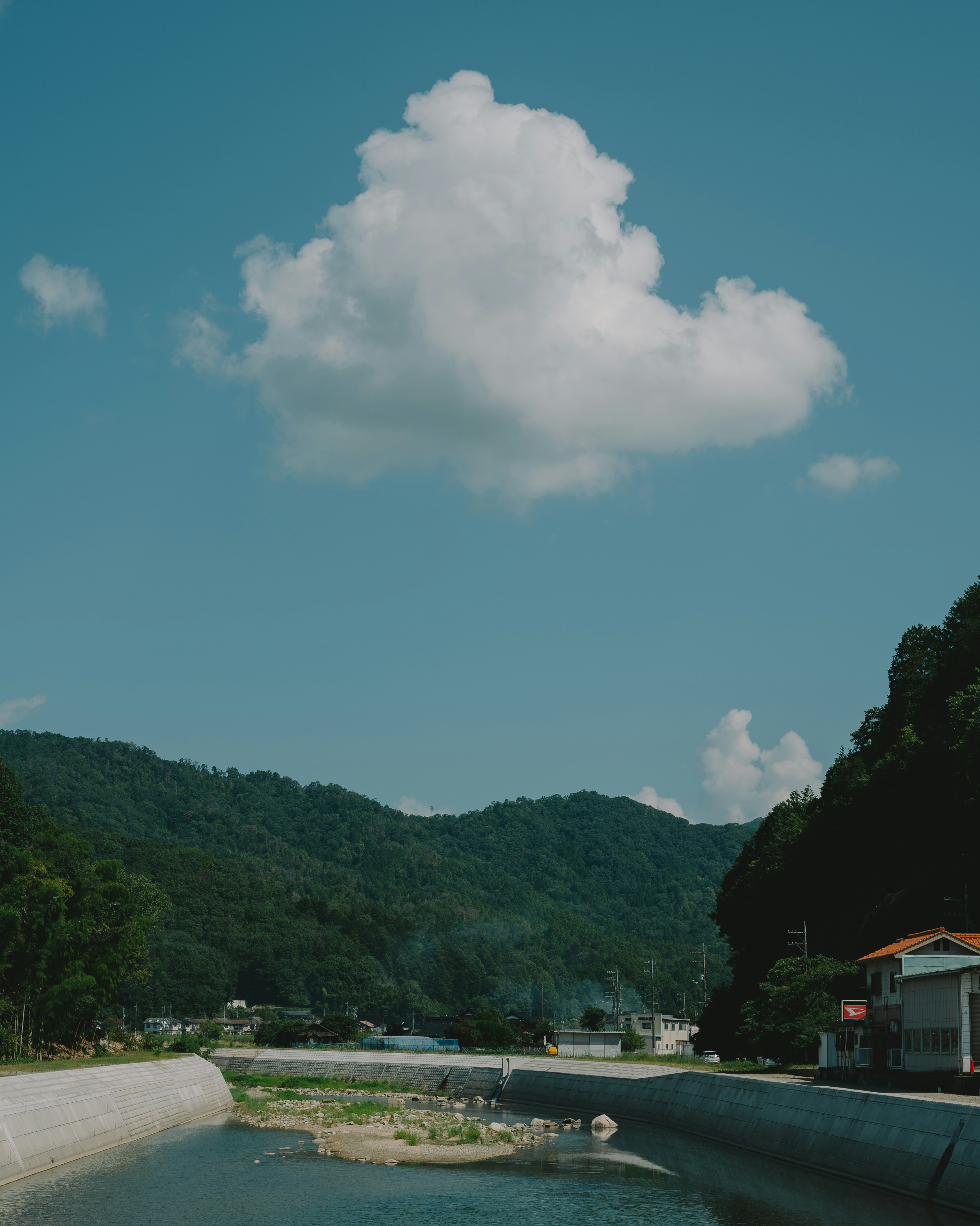 A white cloud floating in a blue sky over green hills