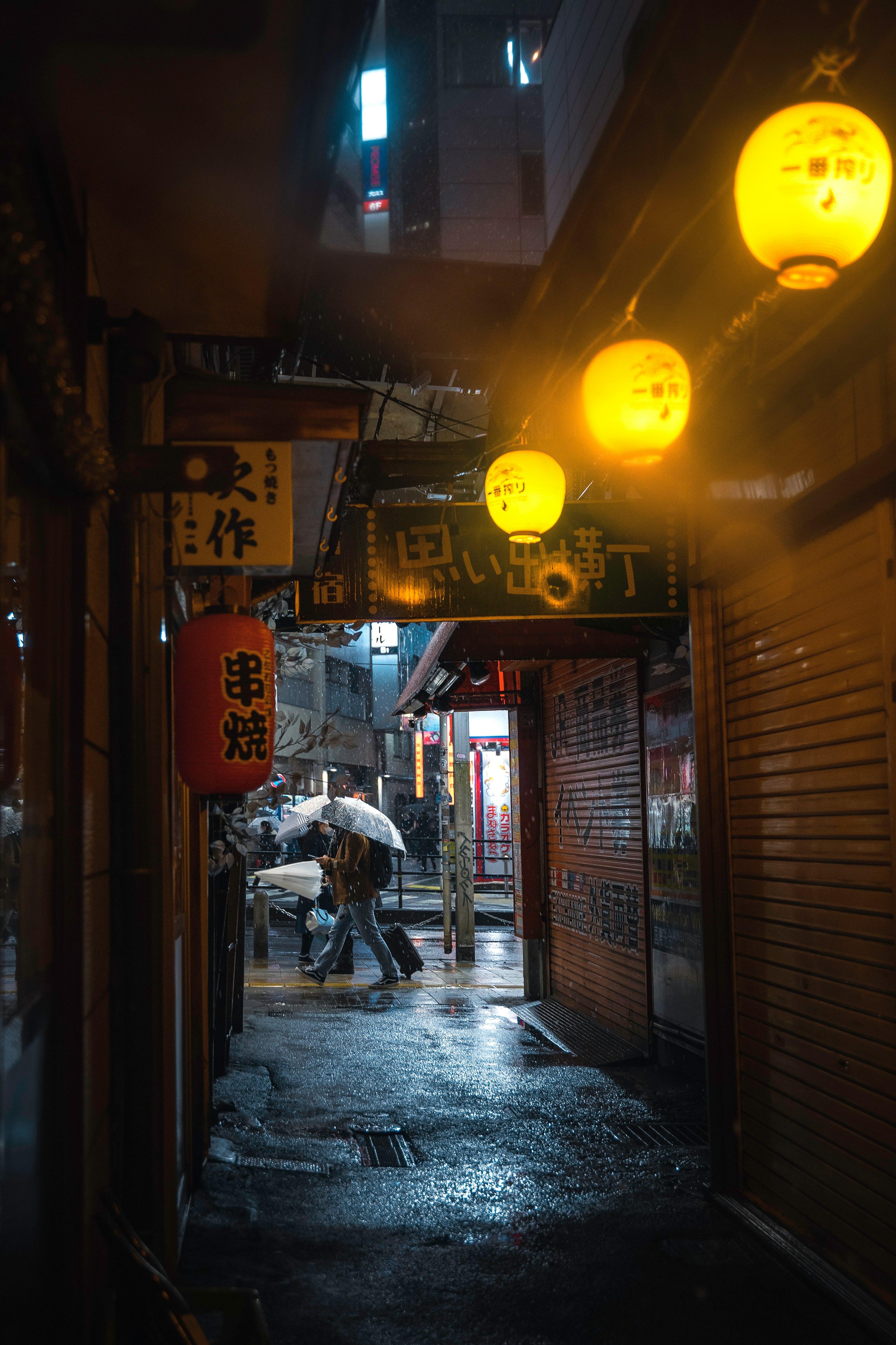 狭い路地に黄色い提灯が並び、雨に濡れた地面が映し出されている