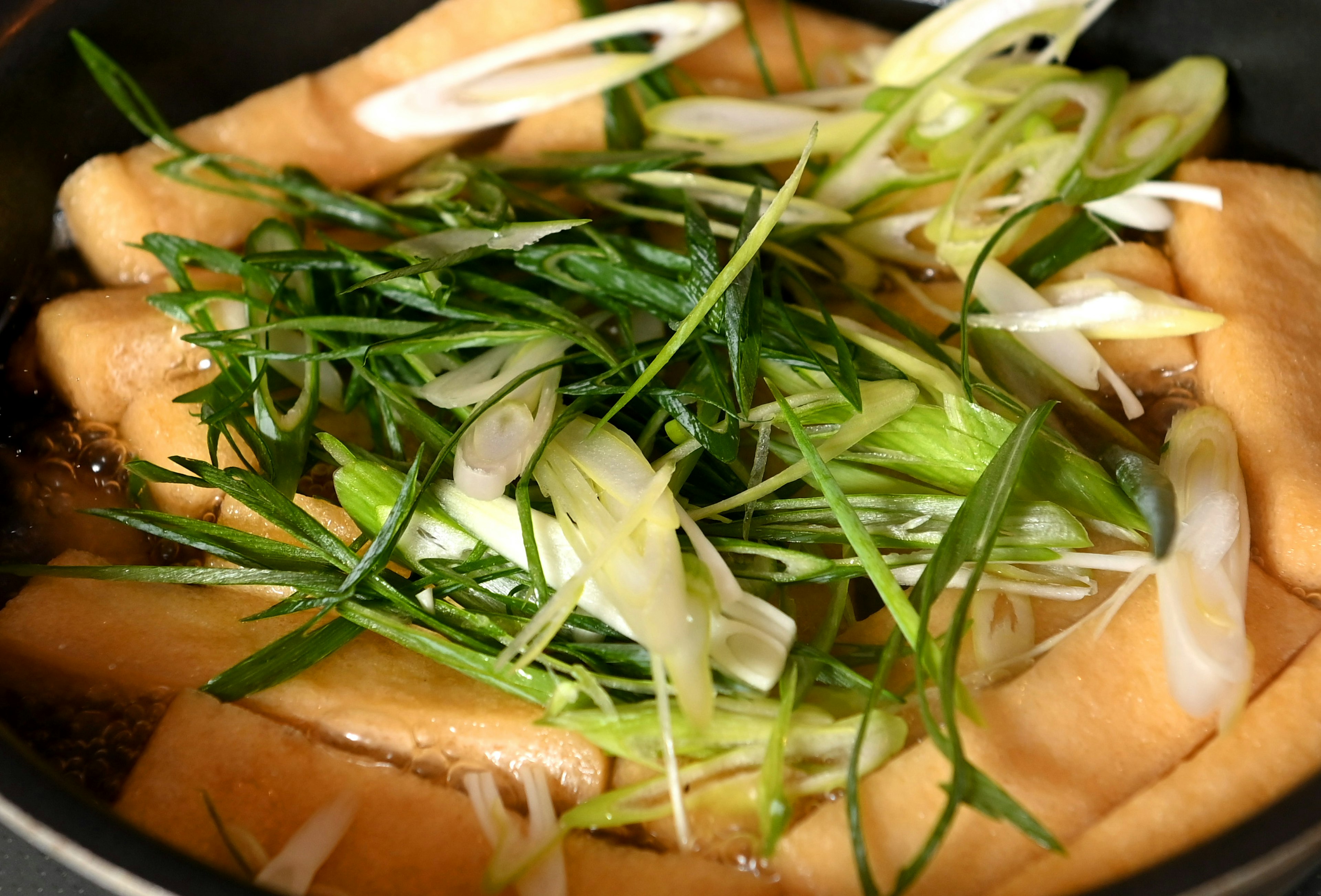 Plat de tofu avec des oignons verts tranchés dans une casserole