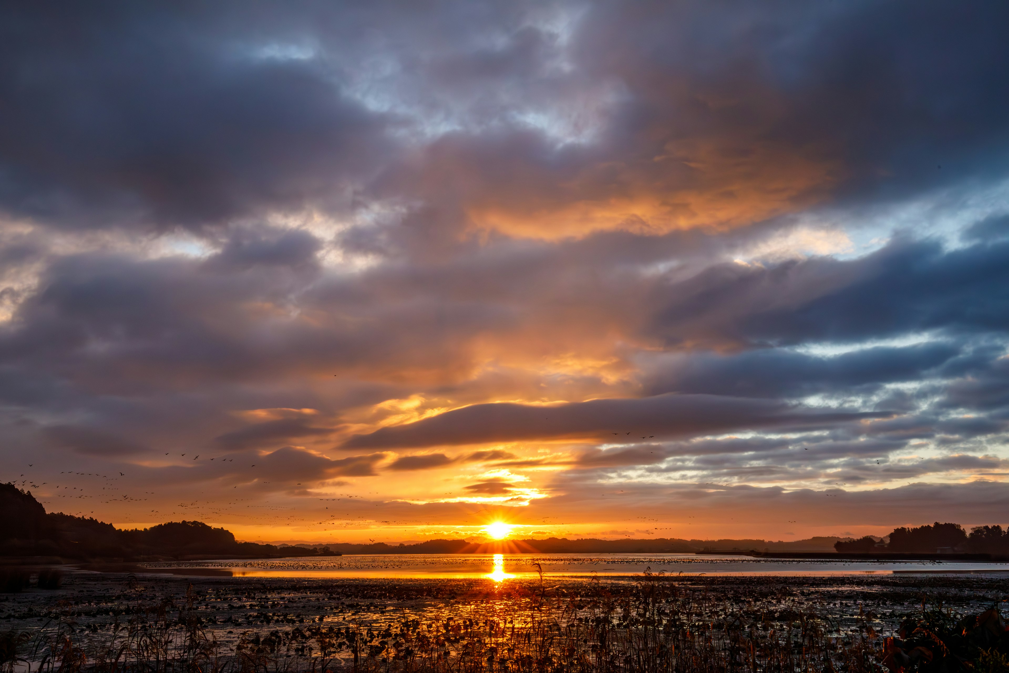 Wunderschöne Landschaft mit Sonnenuntergang der sich im Wasser spiegelt dunkle Wolken und orangefarbener Himmel