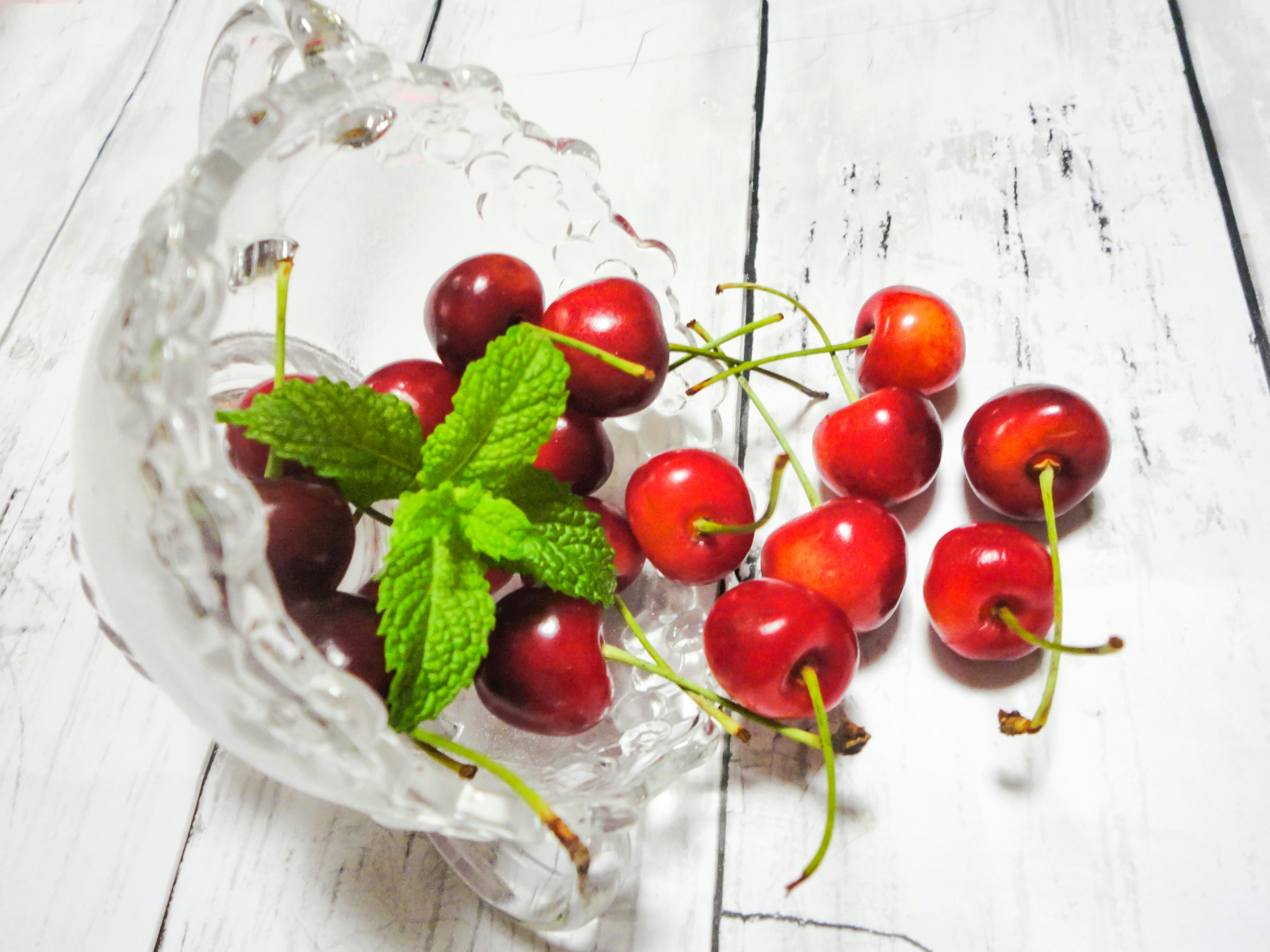 Ciliegie rosse vivaci con foglie di menta in una ciotola di vetro trasparente