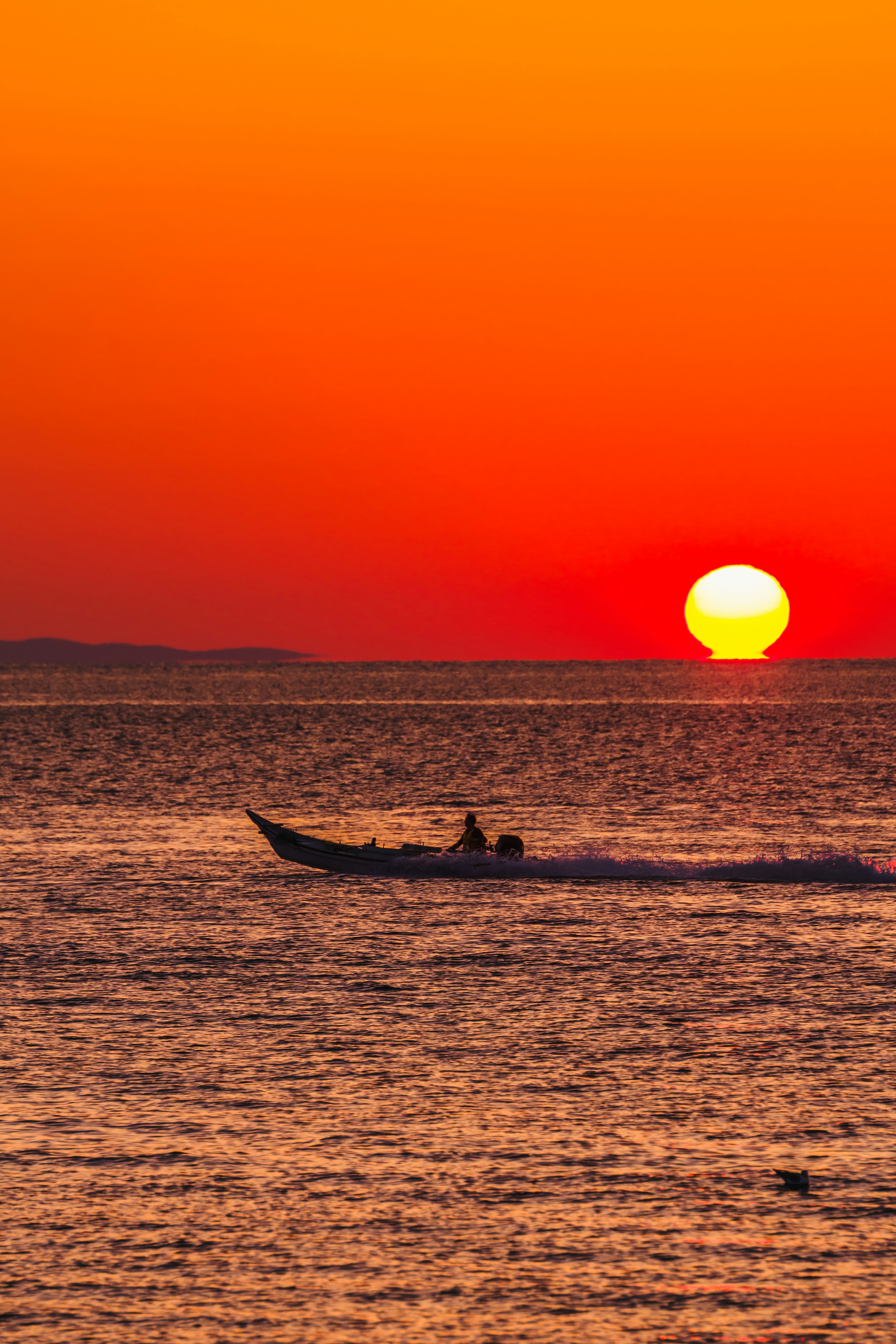 Una barca che naviga sul mare al tramonto con un cielo arancione vivace