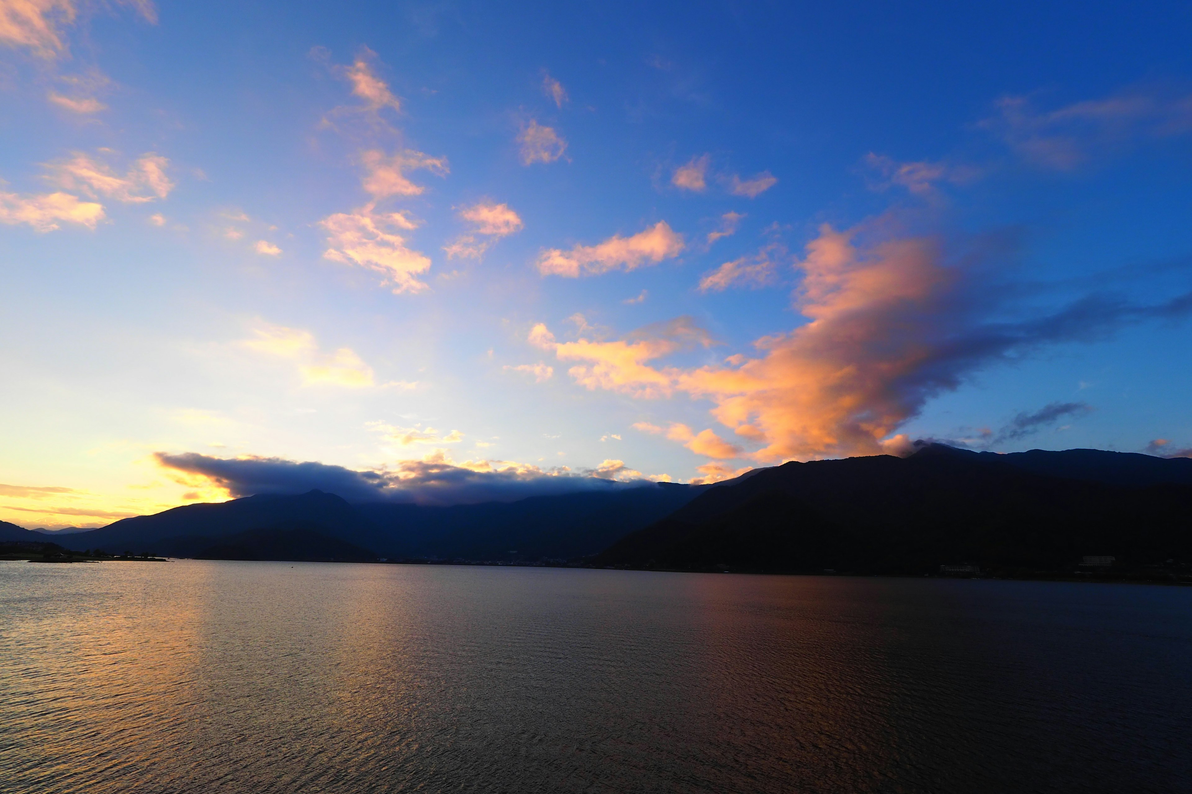 Ruhiger See, der einen Sonnenuntergangshimmel und Berge spiegelt