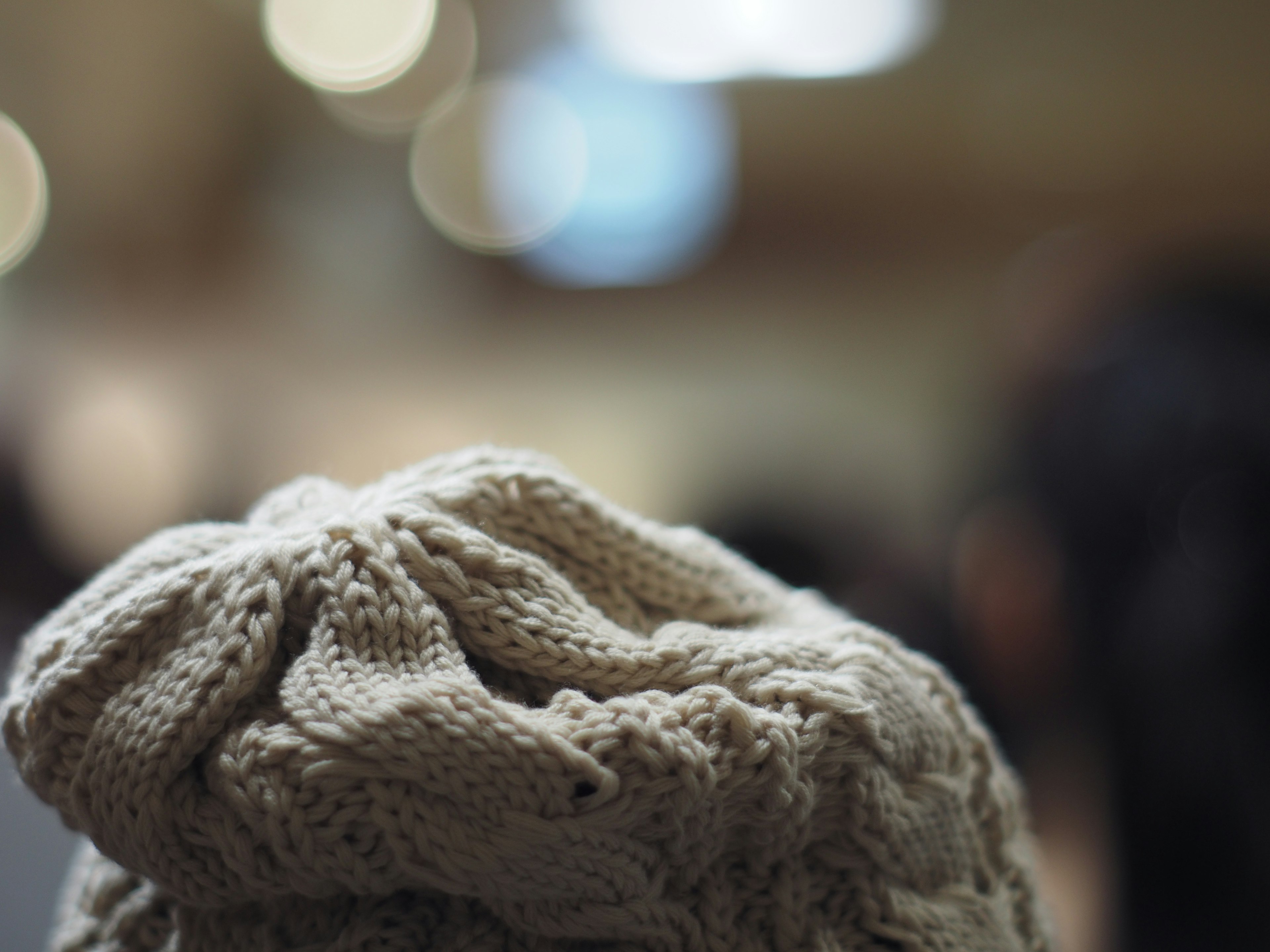 Image showing the back of a beige knitted hat with blurred silhouettes of people in the background