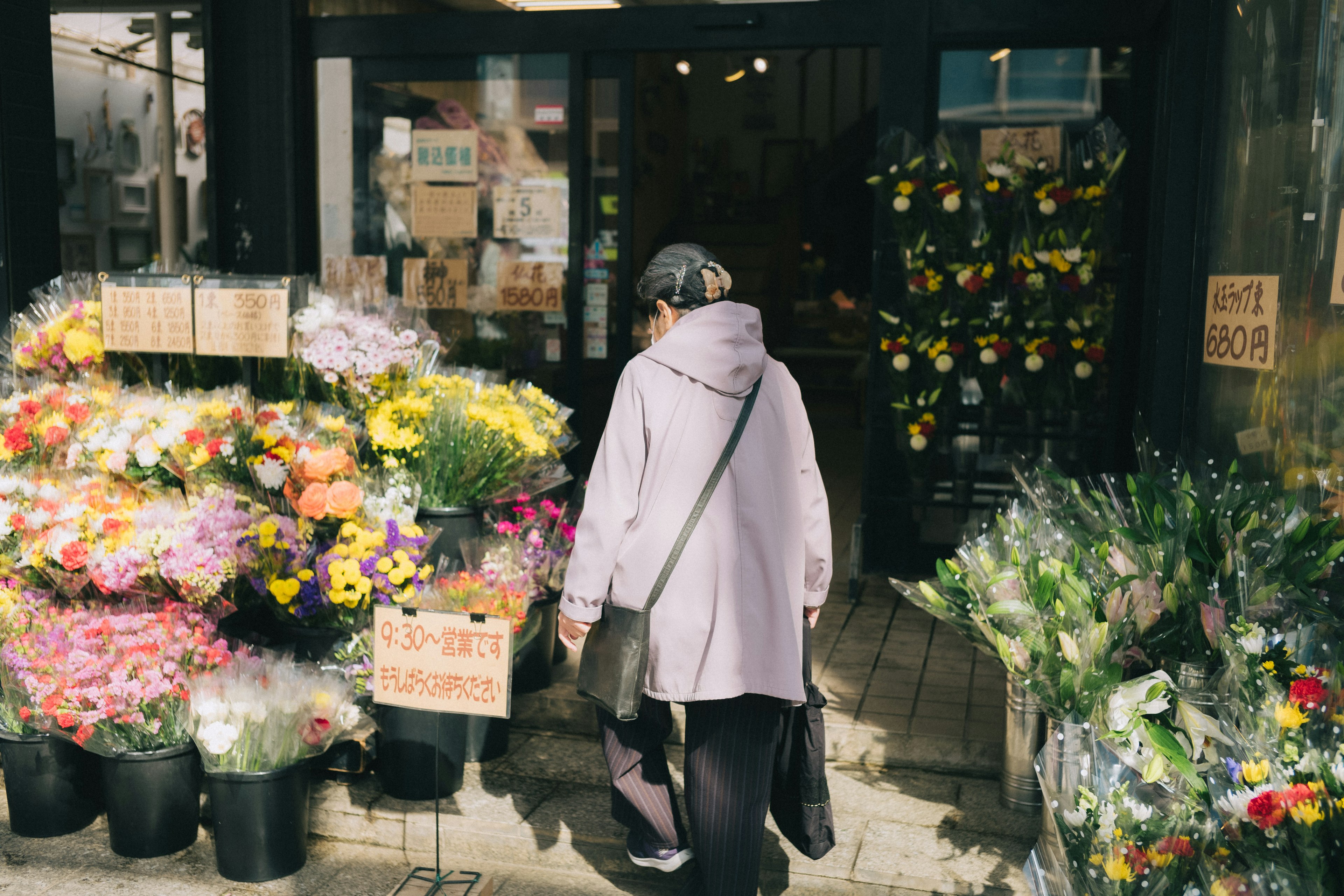 花屋の前を歩く女性 色とりどりの花が並ぶ店