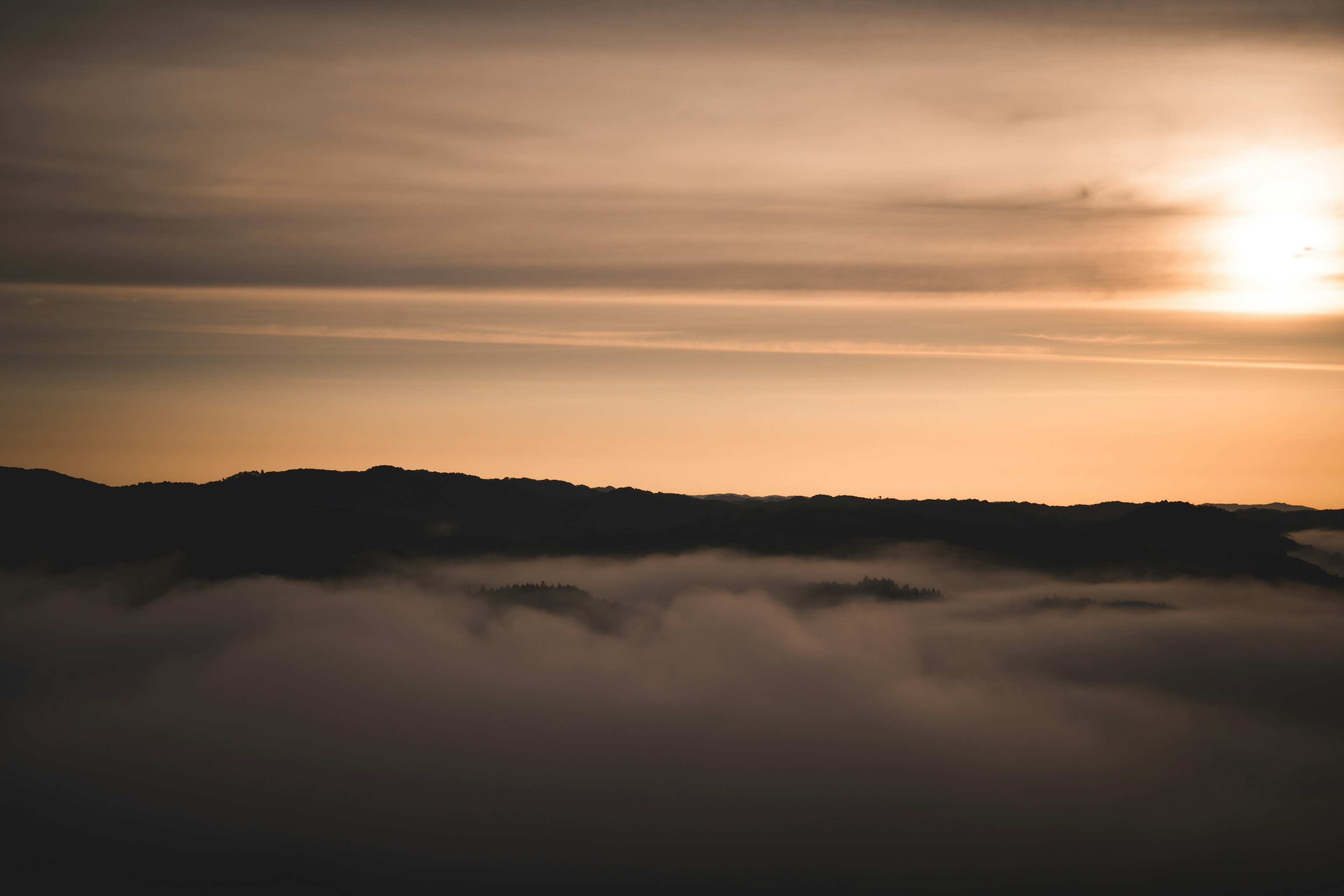 Paisaje montañoso envuelto en niebla con un atardecer sereno