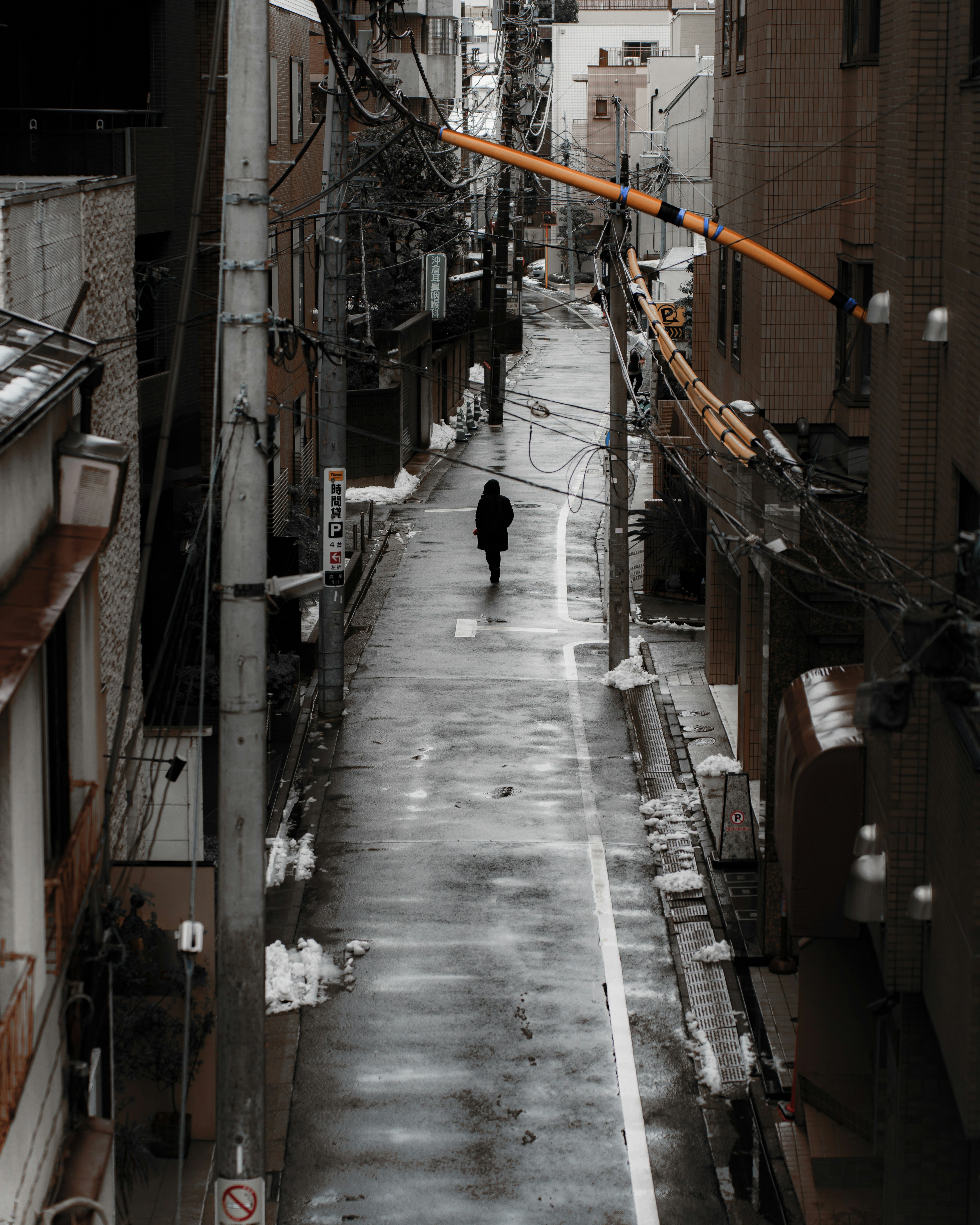 Silueta de una persona caminando en un callejón estrecho empapado de lluvia