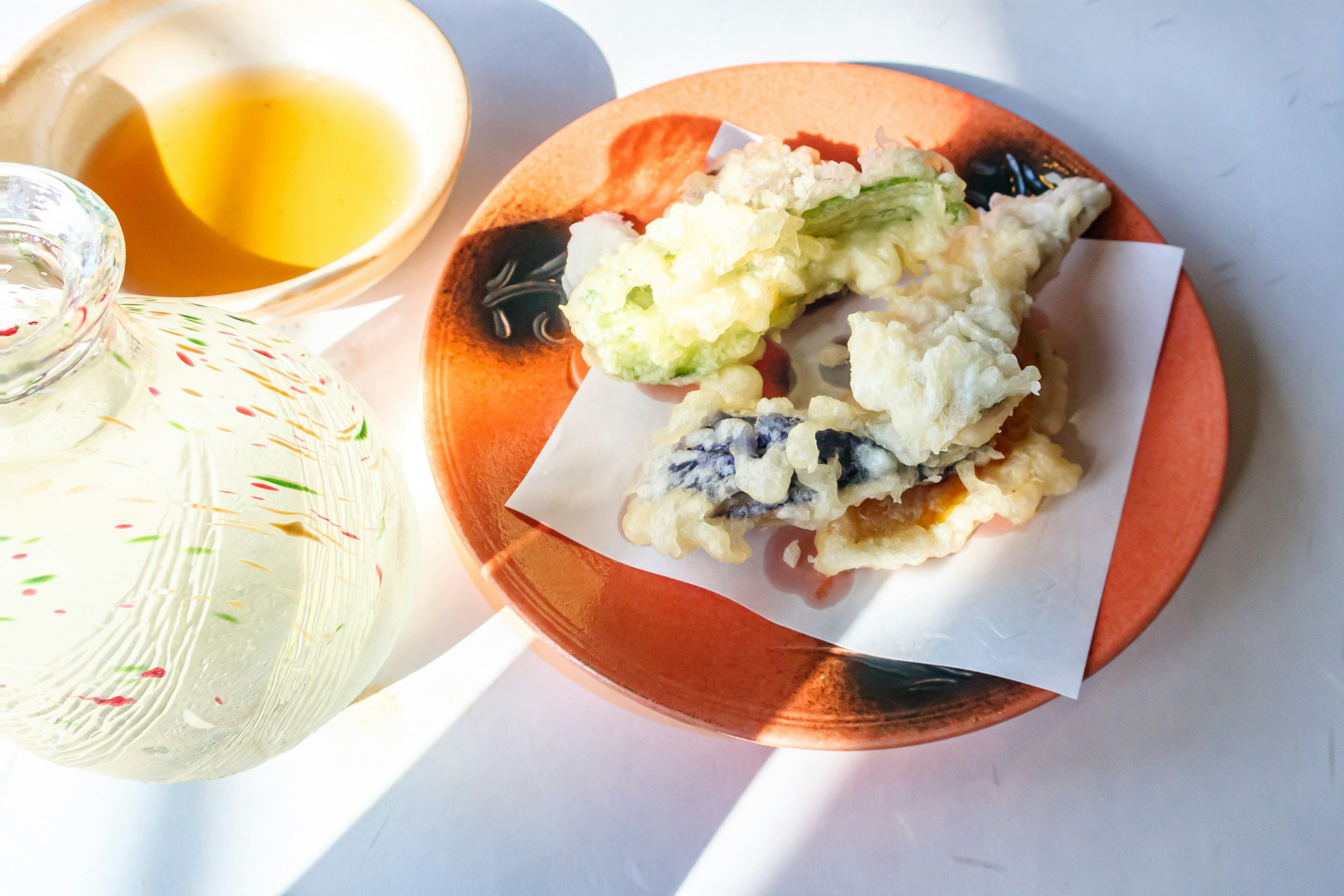 Un piatto con tempura assortita e verdure accanto a una tazza di tè